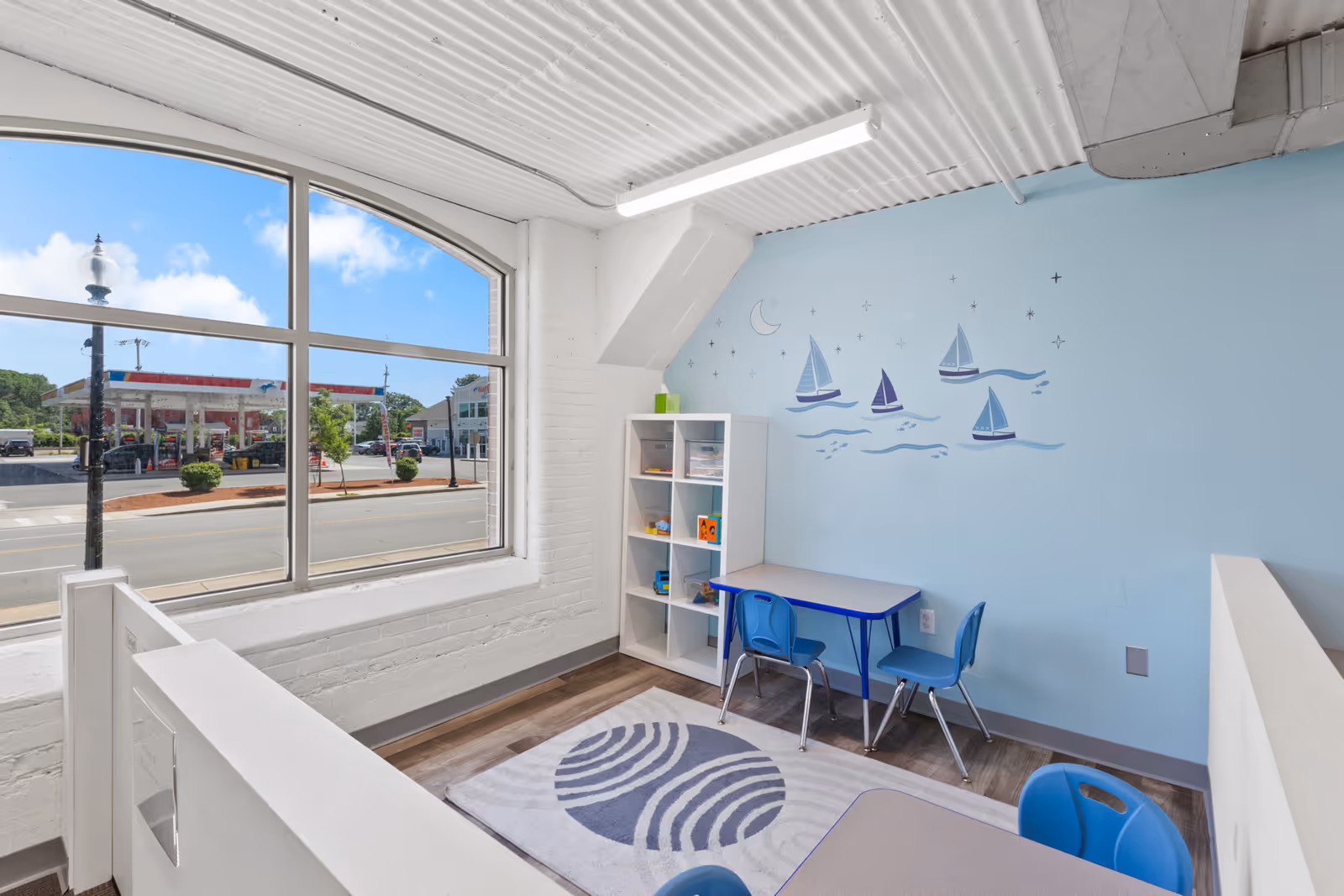 Light-filled playroom with a blue sailboat mural, small table and chairs, and a large window view.