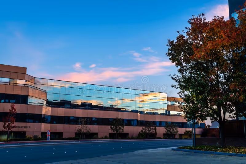 Modern glass-front building with trees along a street at sunset.
