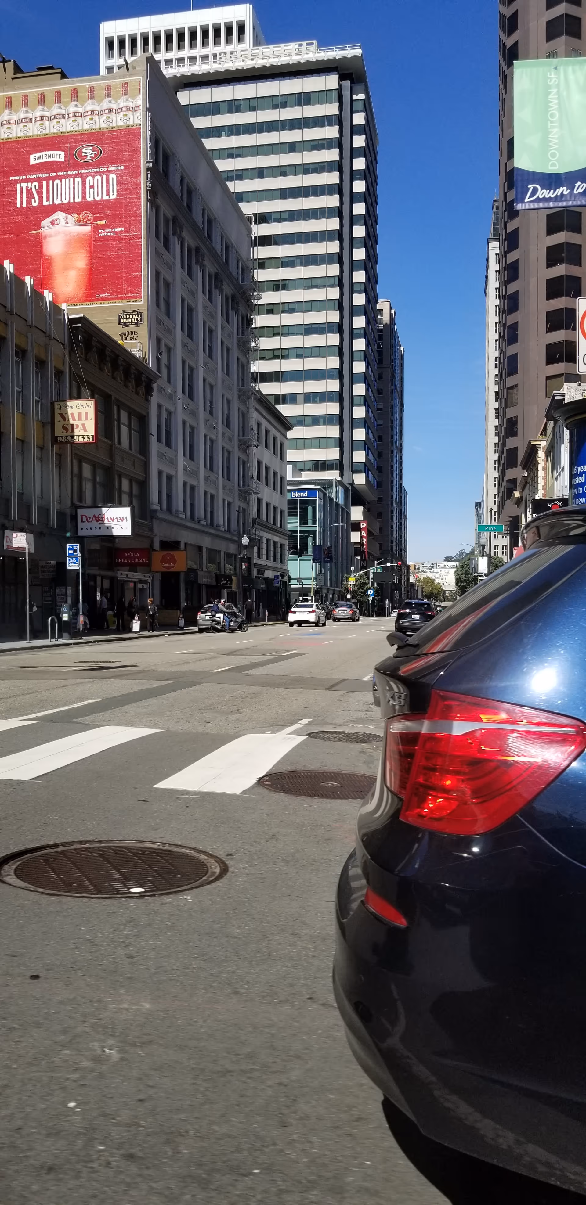 Tall city buildings line a busy street, with a car in the foreground.