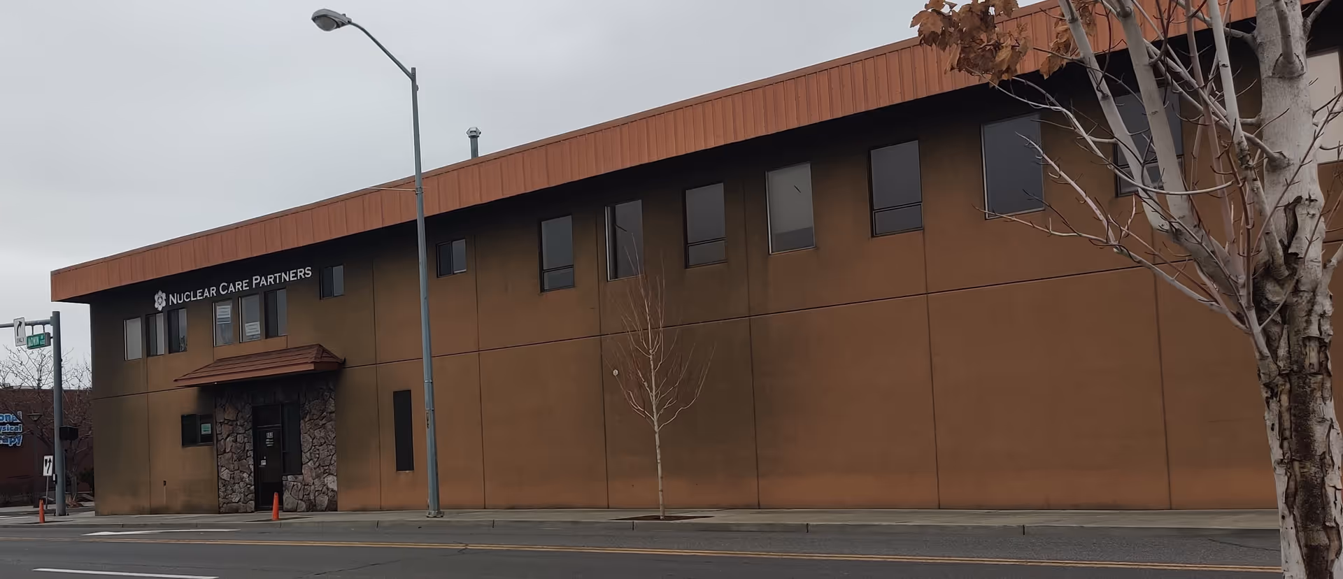 Exterior view of a brown building with Nuclear Care Partners sign along a street.