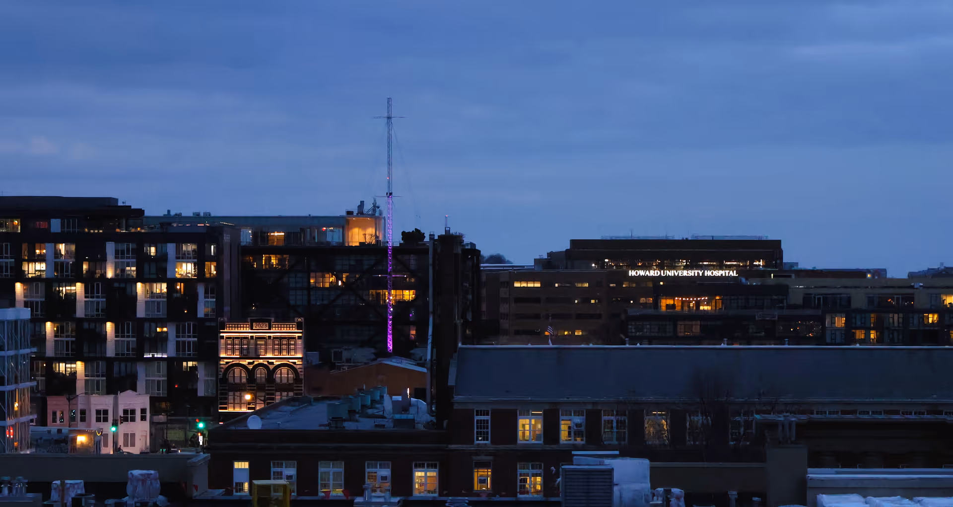 Dusk cityscape featuring distant Howard University Hospital sign above illuminated buildings