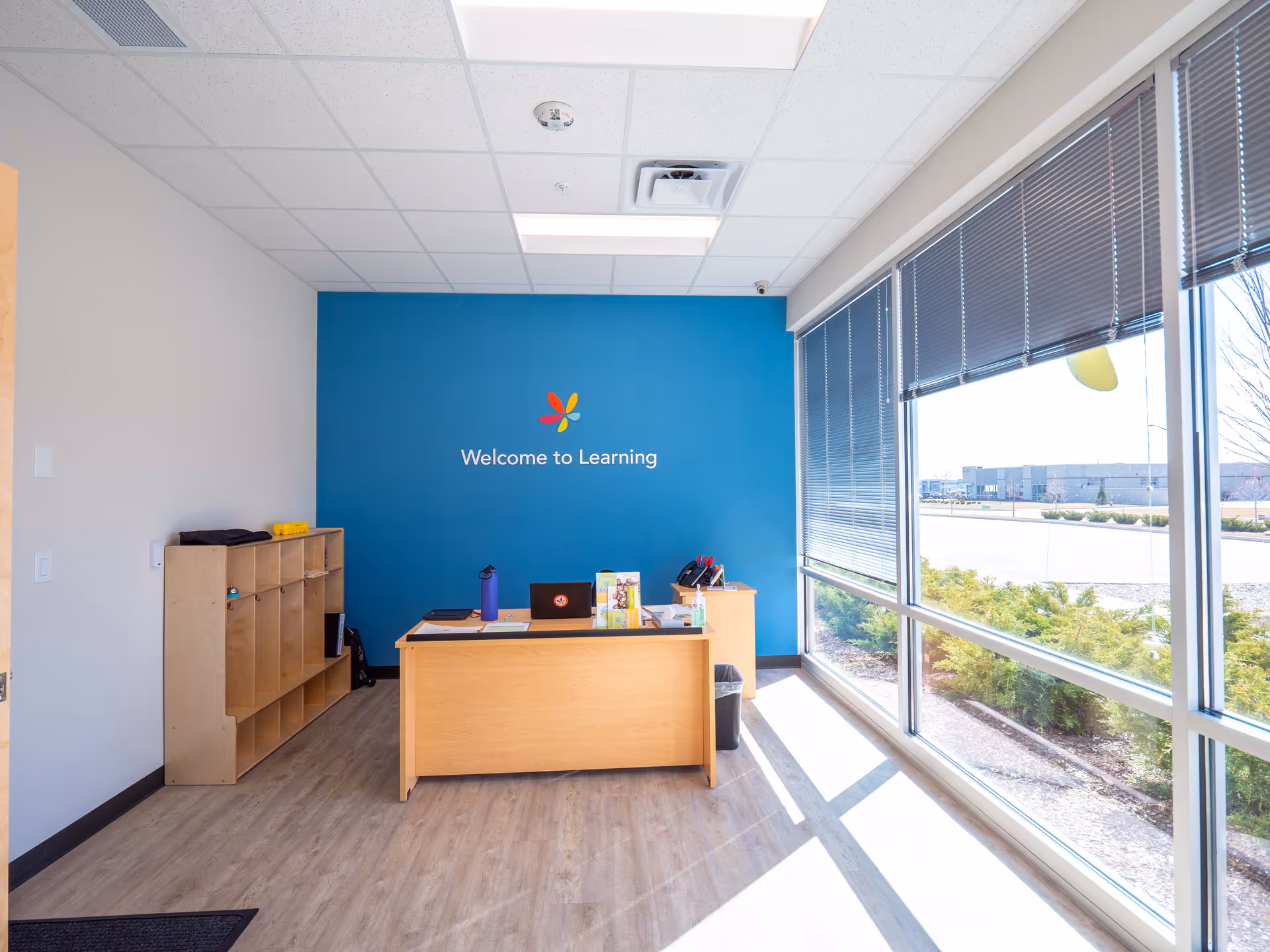 Reception area with a wooden desk, blue learning wall reading Welcome to Learning, and large windows.