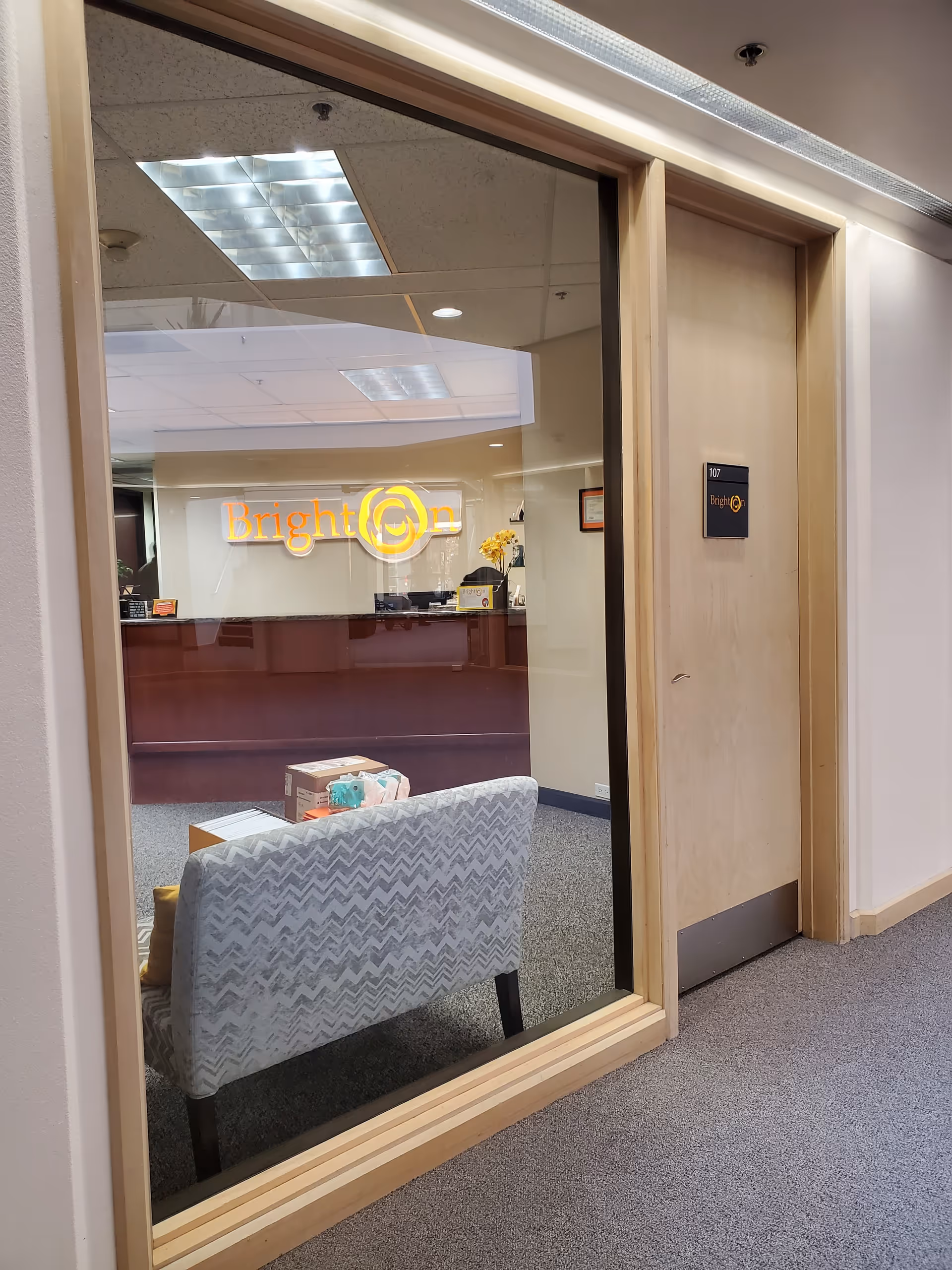 Interior view of Brighton Hospice reception with glass wall, sofa, and front desk signage.