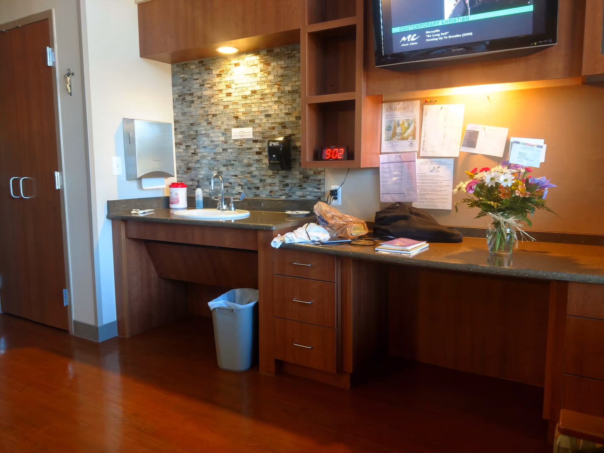 Wood-finished kitchenette with sink, tiled backsplash, and a bouquet on the counter.