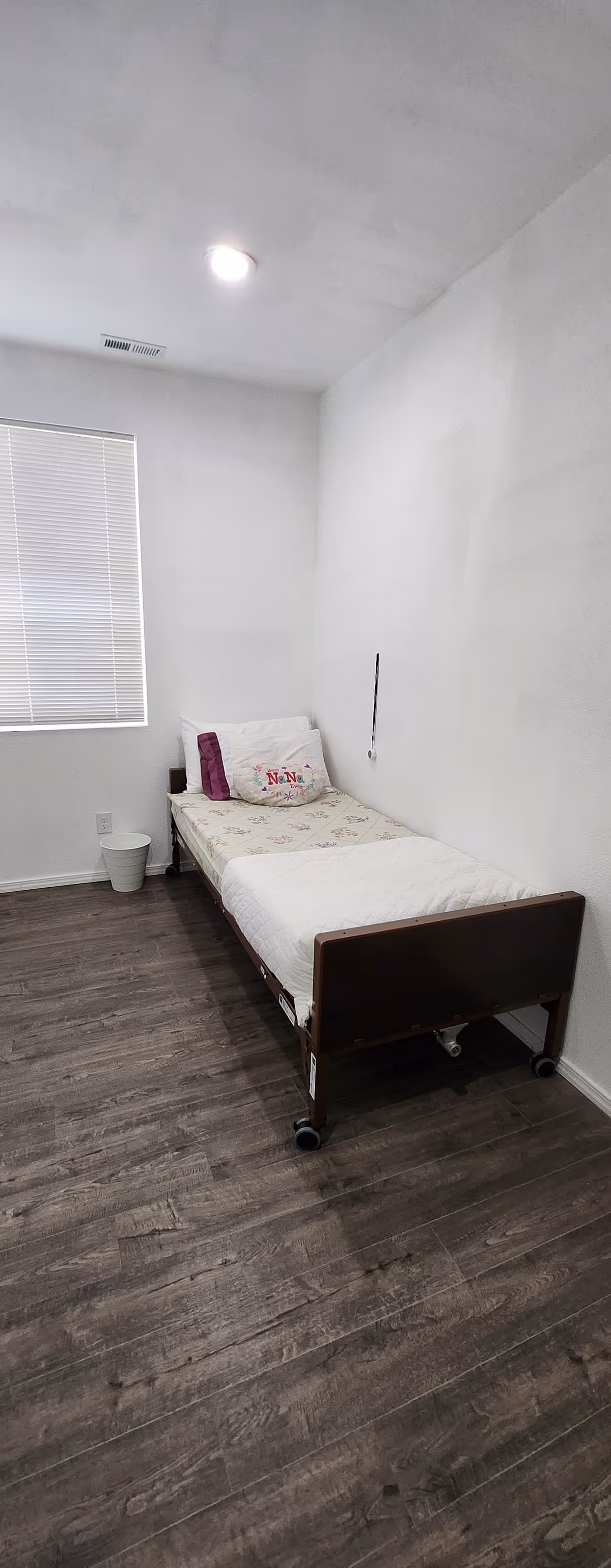 A sparsely furnished bedroom with a single bed, window, and minimal decor.
