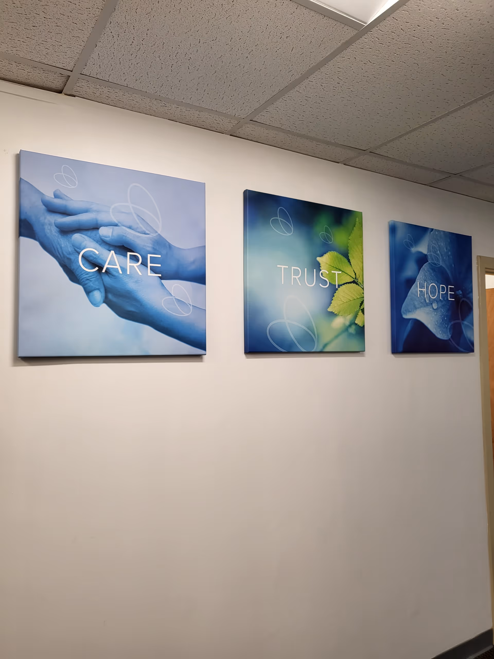 Three framed wall art pieces with CARE, TRUST, HOPE hang in a hallway.