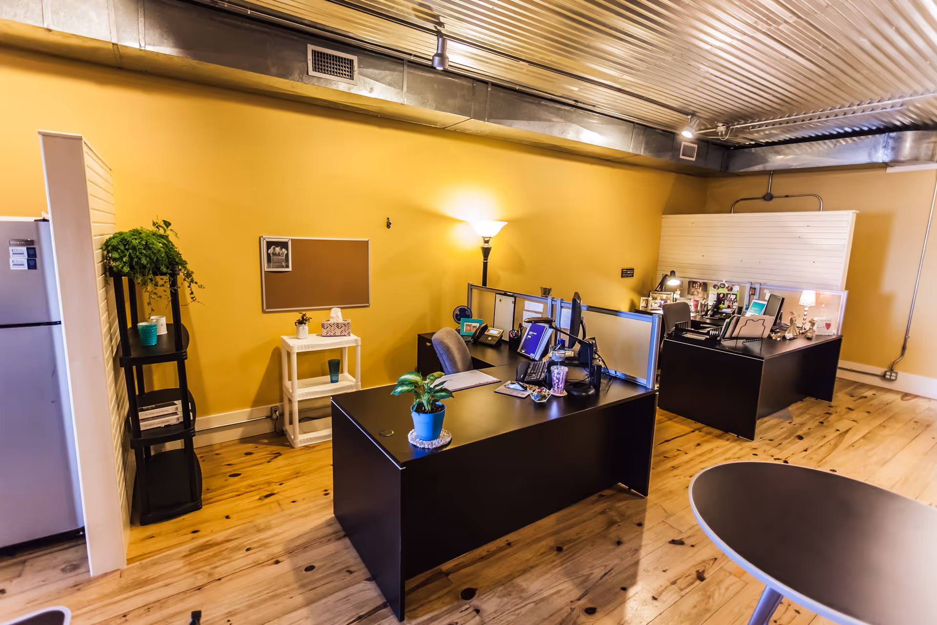 Open office area with desks, cubicles, warm yellow walls, and wooden flooring.