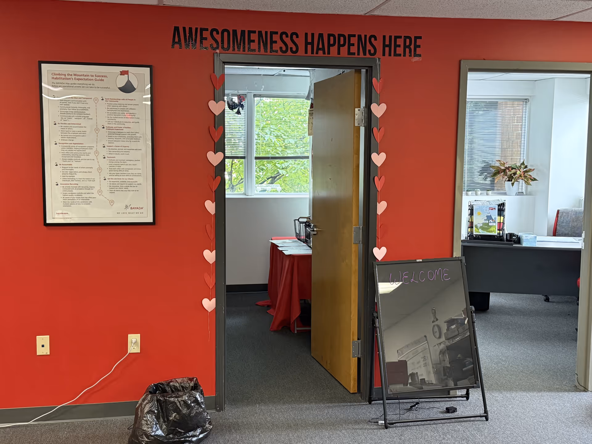 Bright red wall lobby area with doorway, heart garlands, and welcome board.