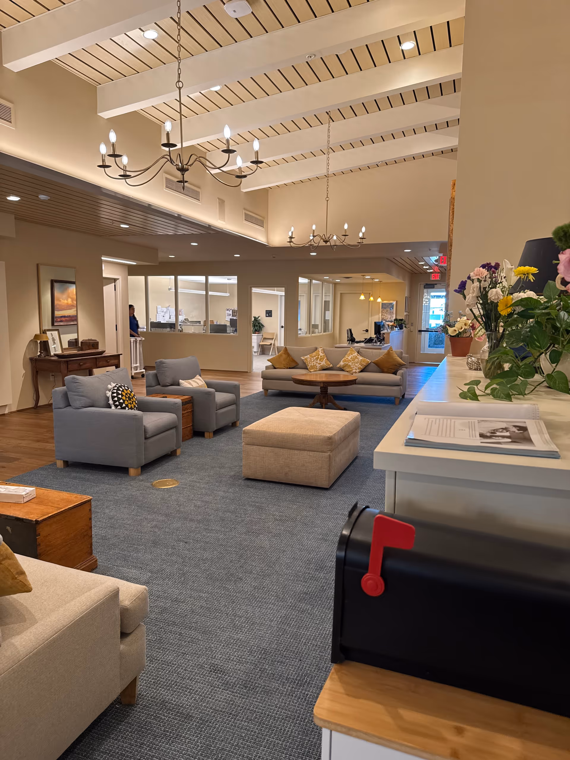 Bright, spacious lounge with blue seating, chandeliers, and a front desk in a hospice lobby.