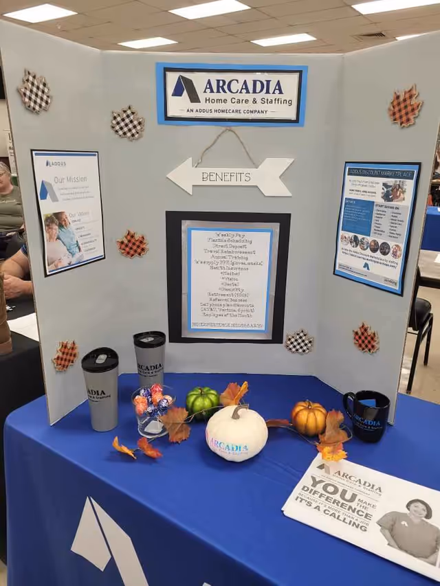 Arcadia Home Care booth at an indoor expo with display boards and a blue table.