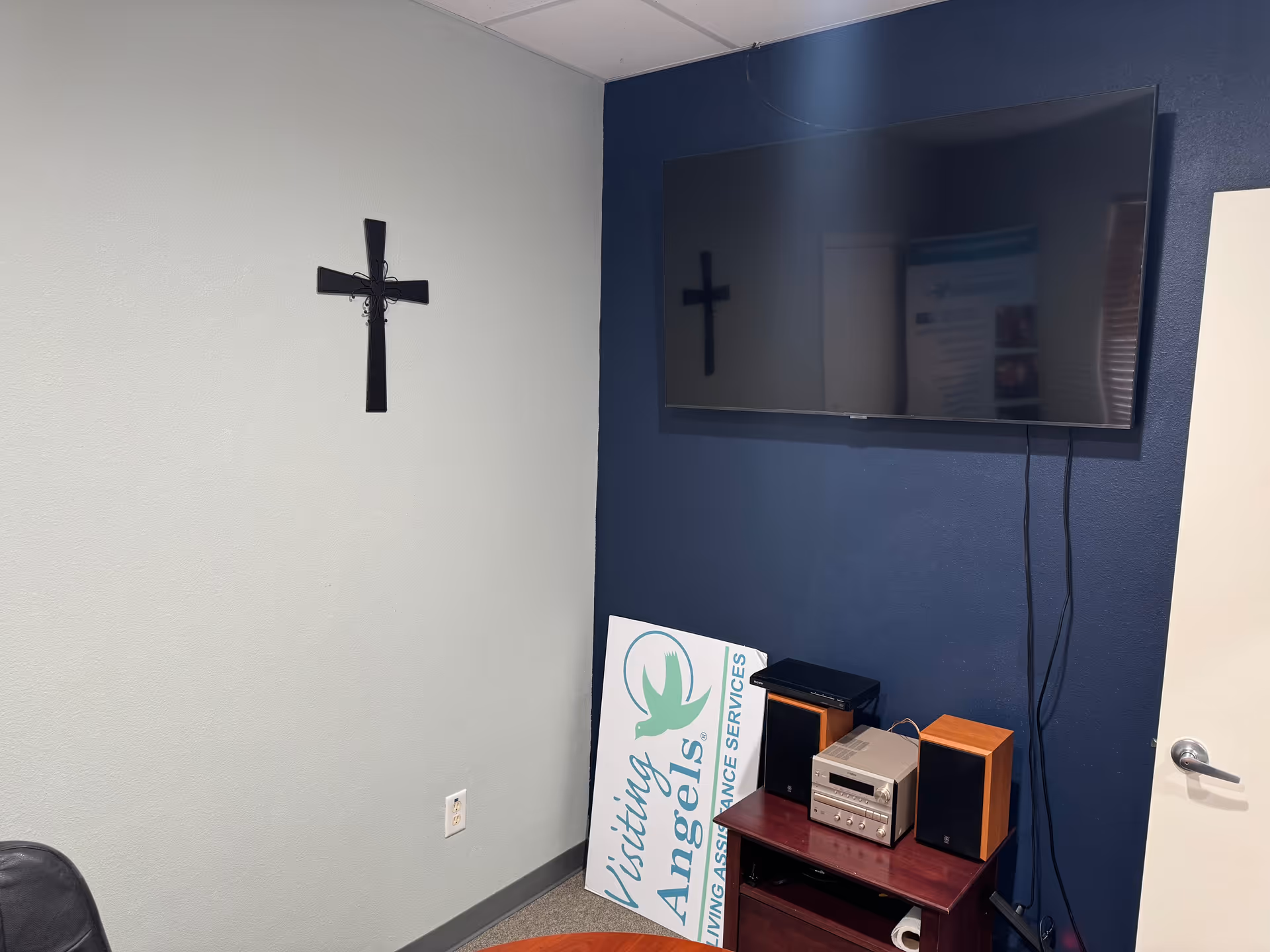 Interior room with a wall-mounted TV, a cross on the wall, and electronics.