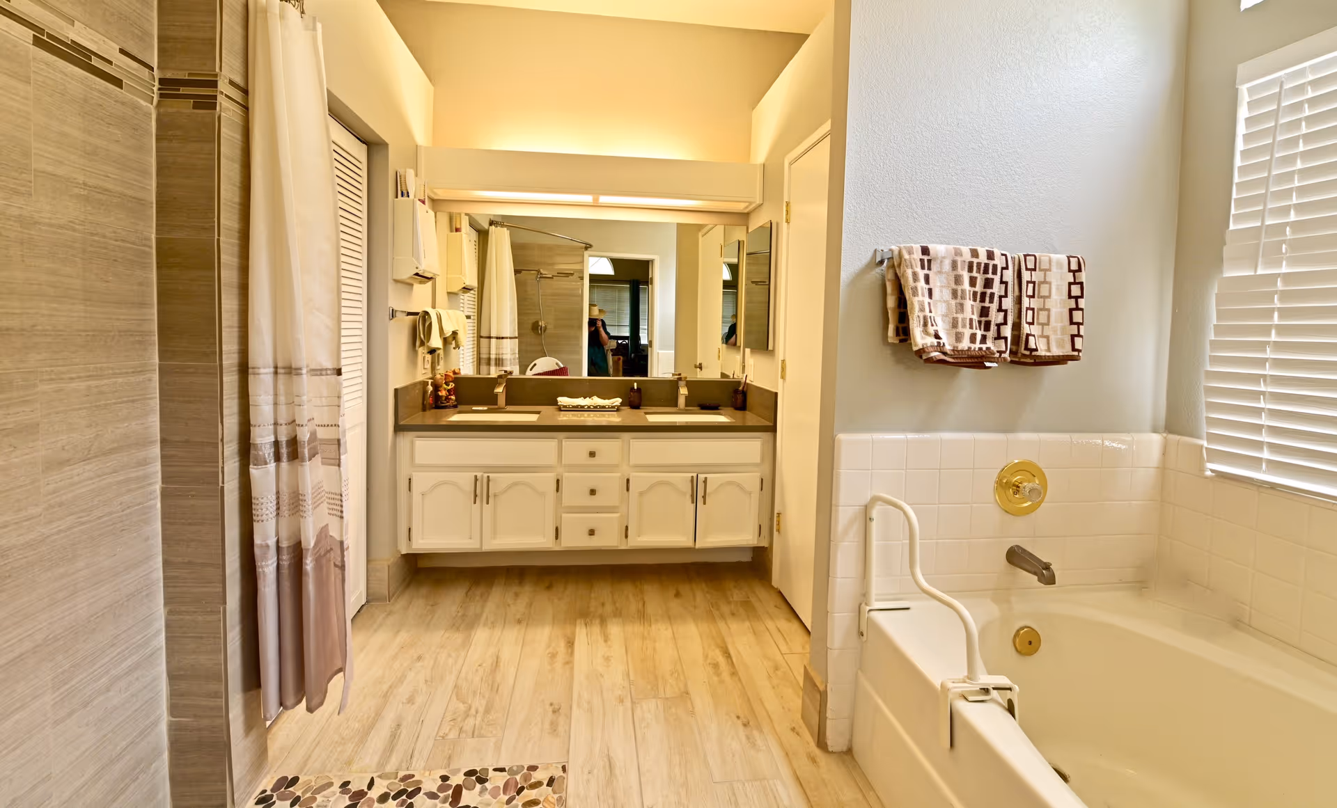 A clean bathroom in a senior living facility with a double vanity, tub, and shower curtain.
