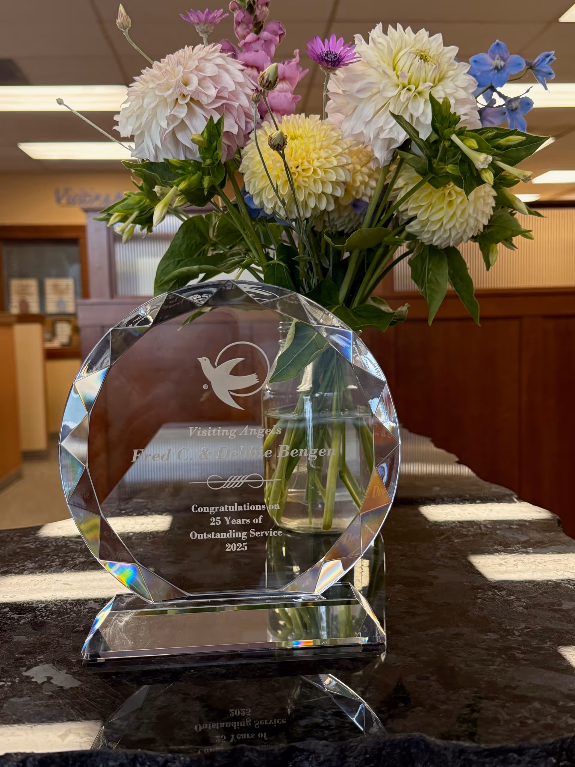 Crystal award and vibrant flower arrangement sit on a marble counter in a facility lobby.