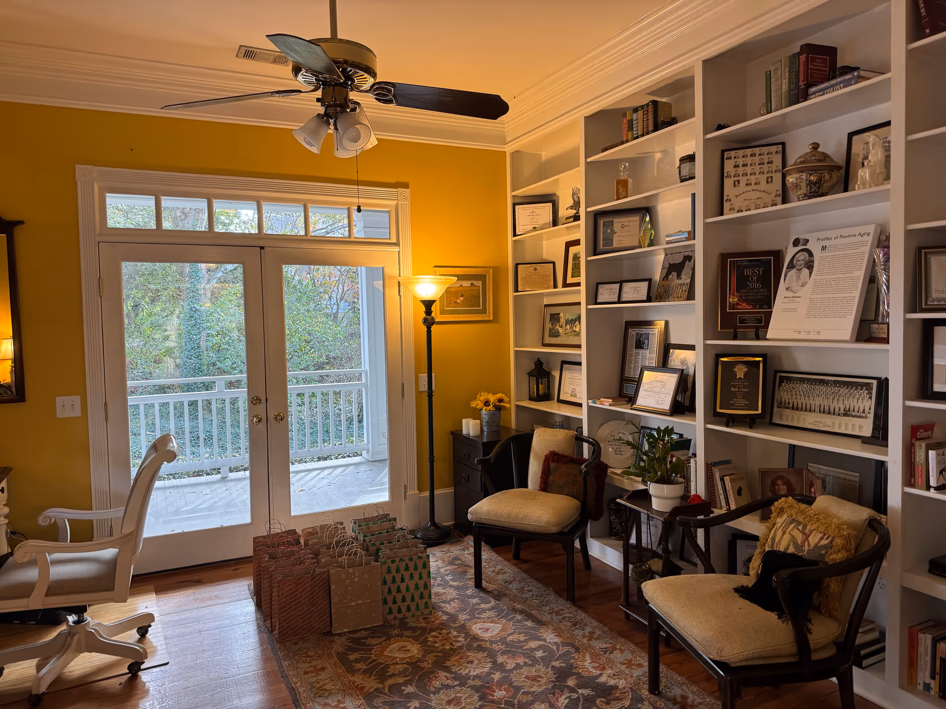 Yellow-walled living room with French doors, built-in bookshelves, chairs, and a patterned rug.