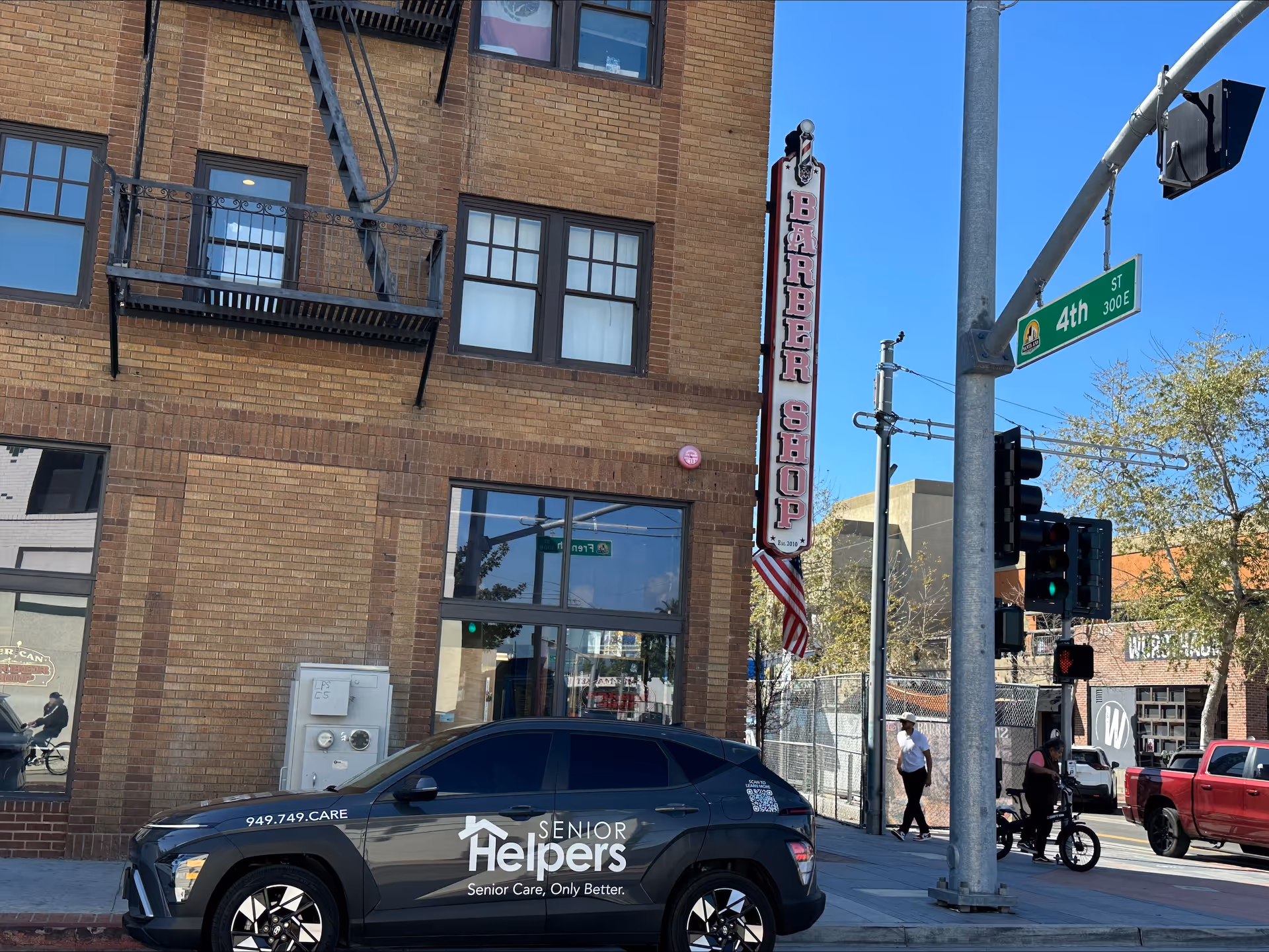 Barber shop storefront on brick building with Senior Helpers car parked on street.