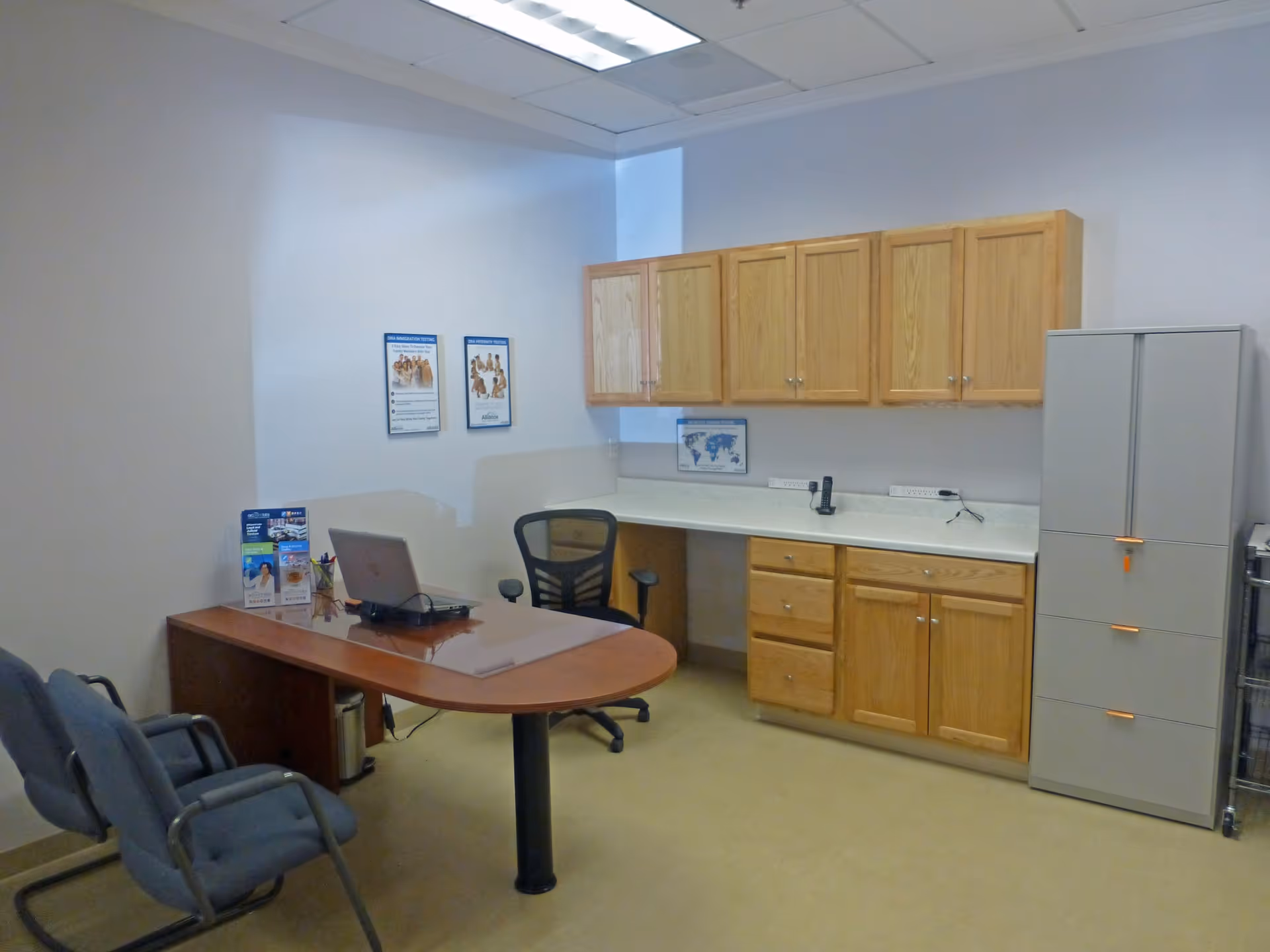 Office area with curved wooden desk, laptop, upper and lower cabinets, and gray filing cabinet.
