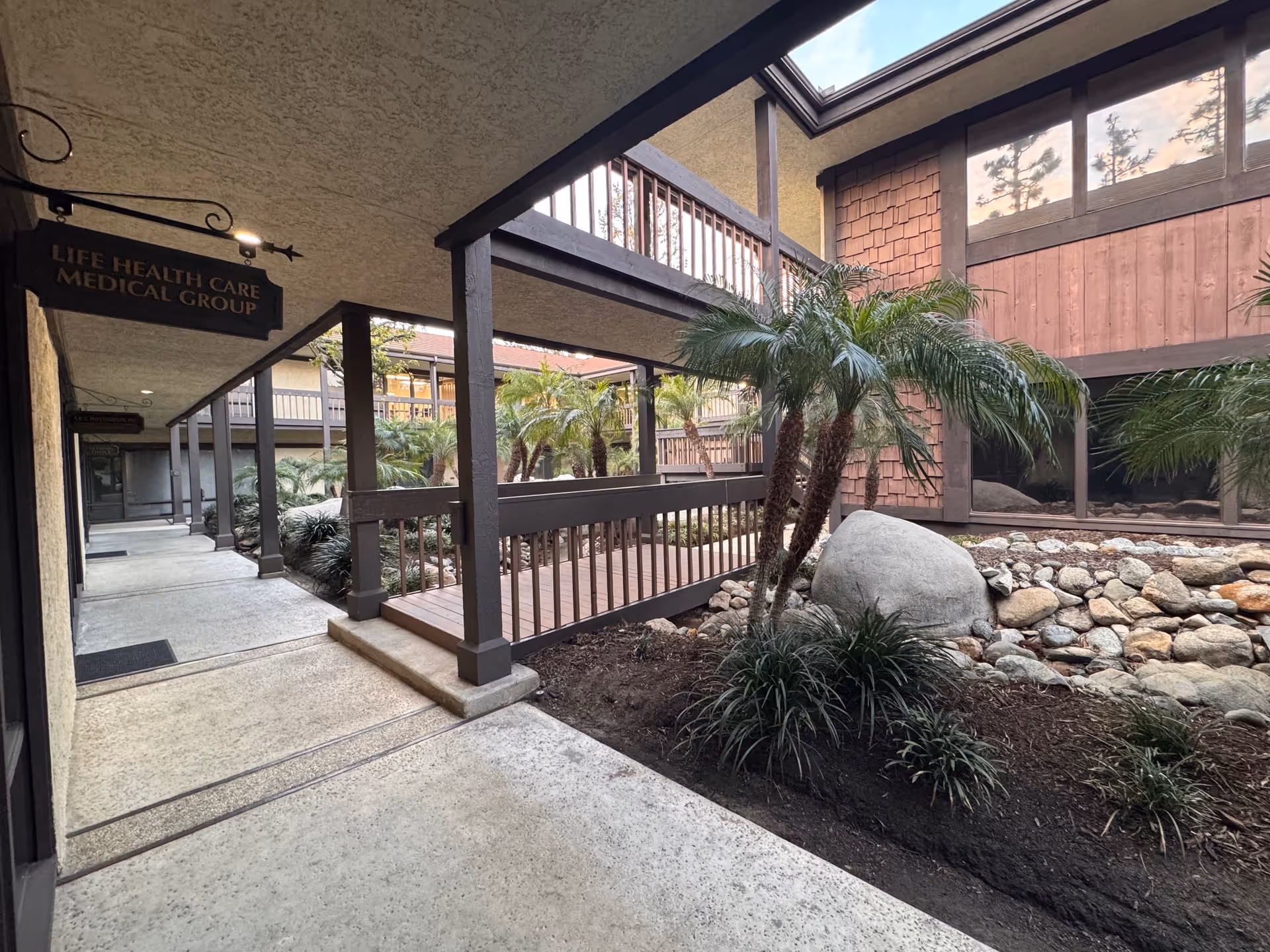 Outdoor walkway with railing, palm trees, and rock garden at Life Health Care Medical Group.
