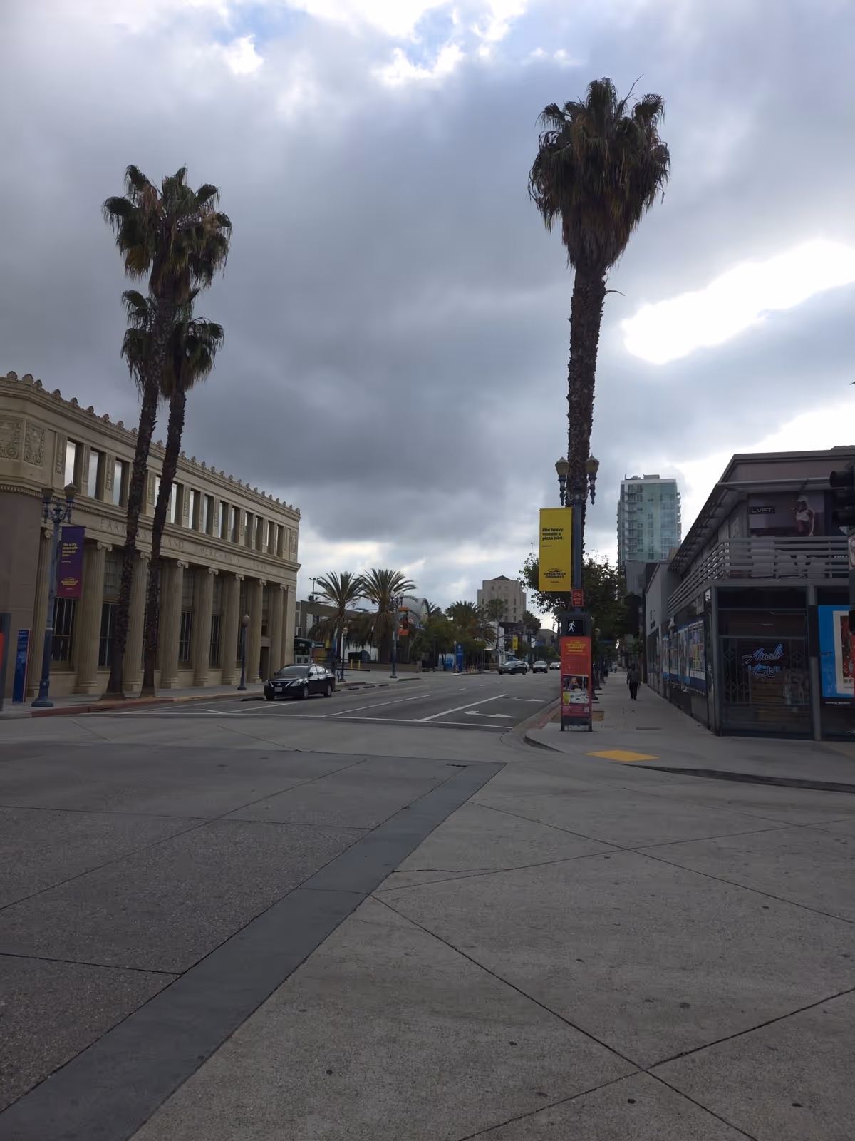 Urban street scene with tall palm trees, historic buildings, and a cloudy sky.