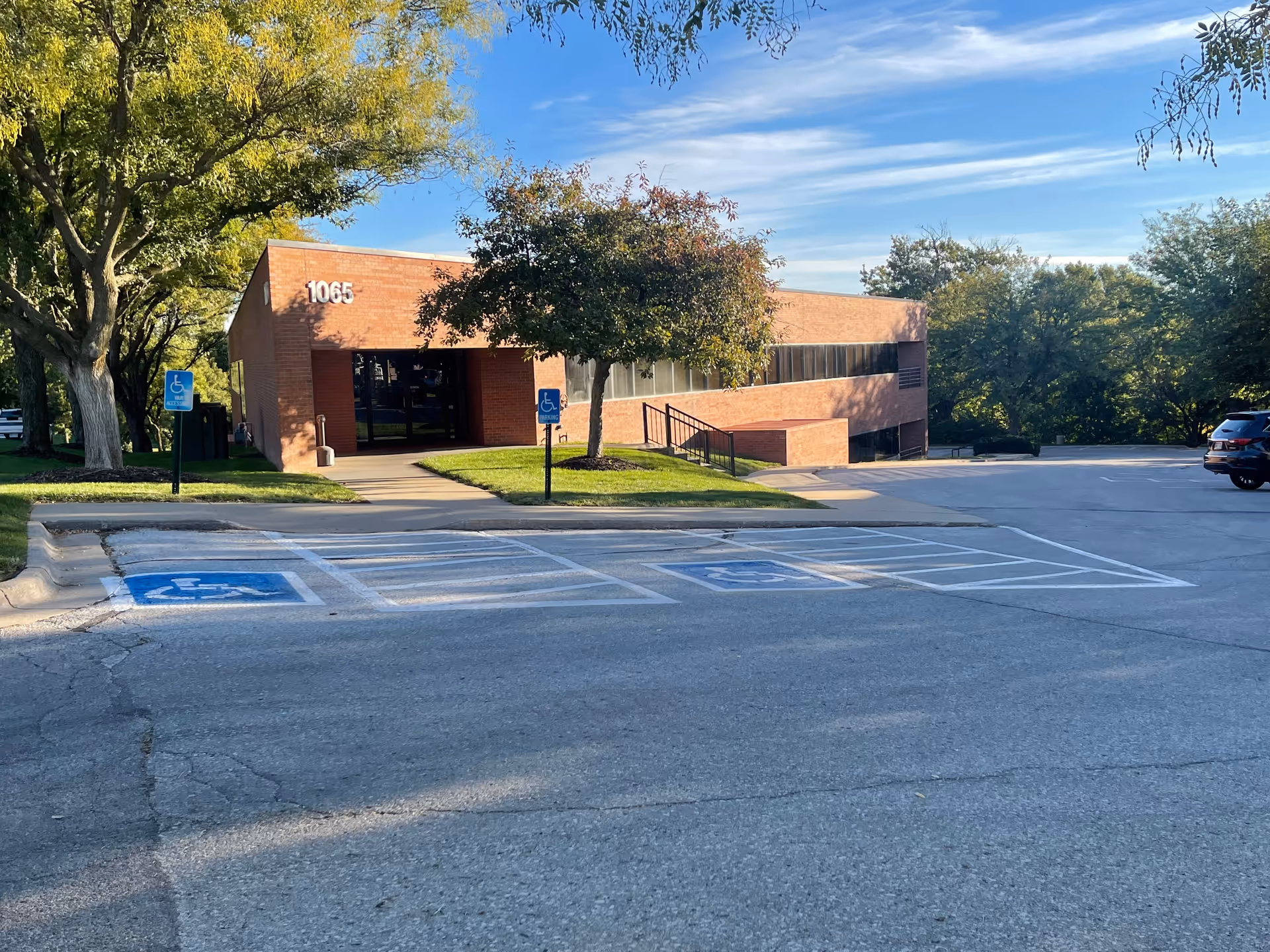 Brick senior care building with sidewalk, ramp, and accessible parking in a sunny lot.