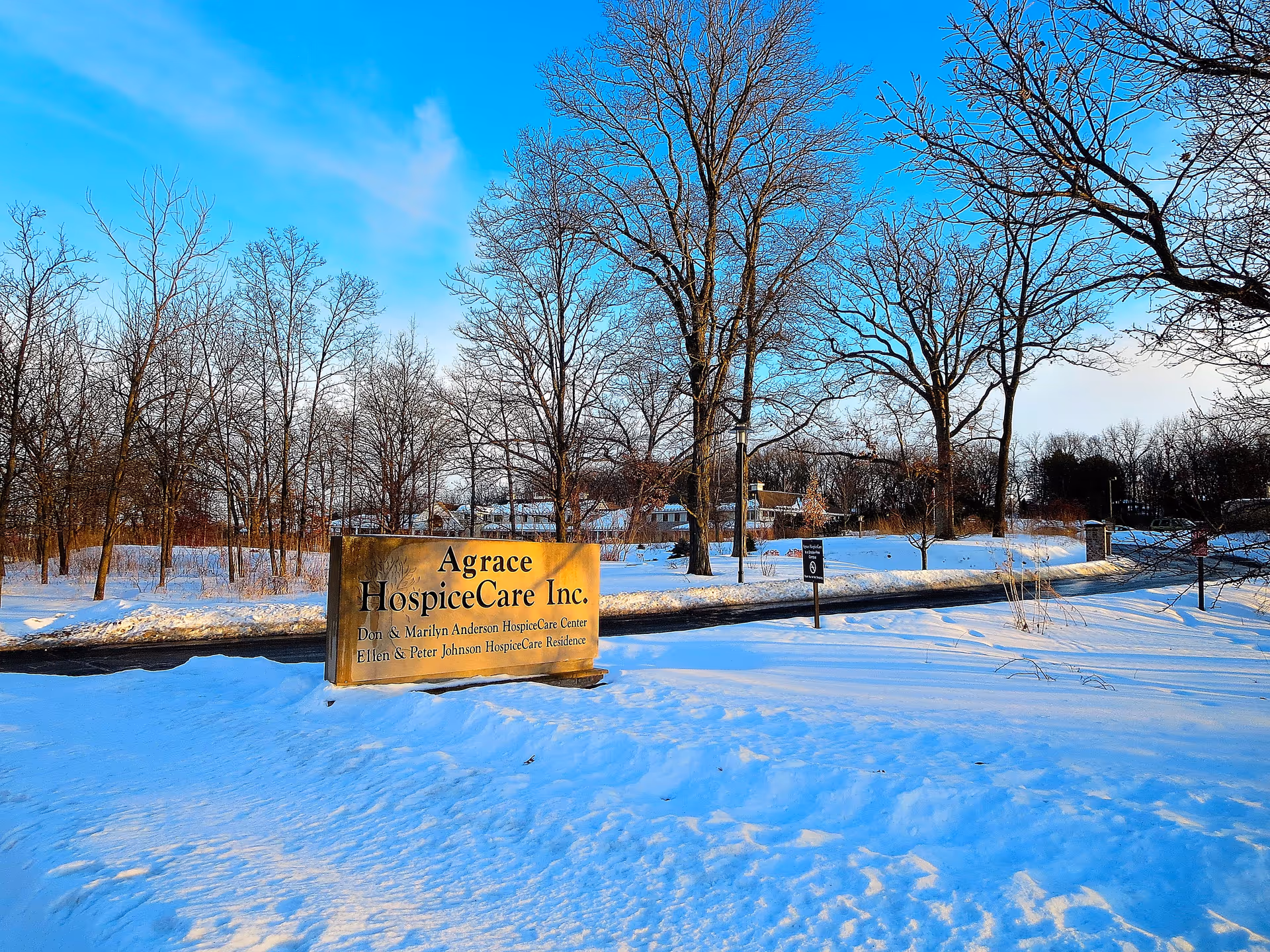 Snowy outdoor scene with a sign reading Agrace HospiceCare Inc. among leafless trees.
