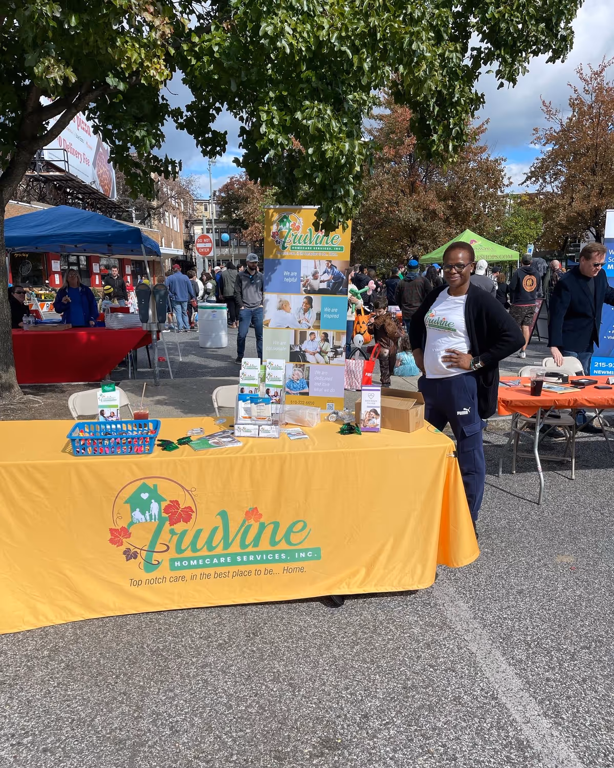 A TruVine Homecare Services table at an outdoor street fair with staff and attendees.