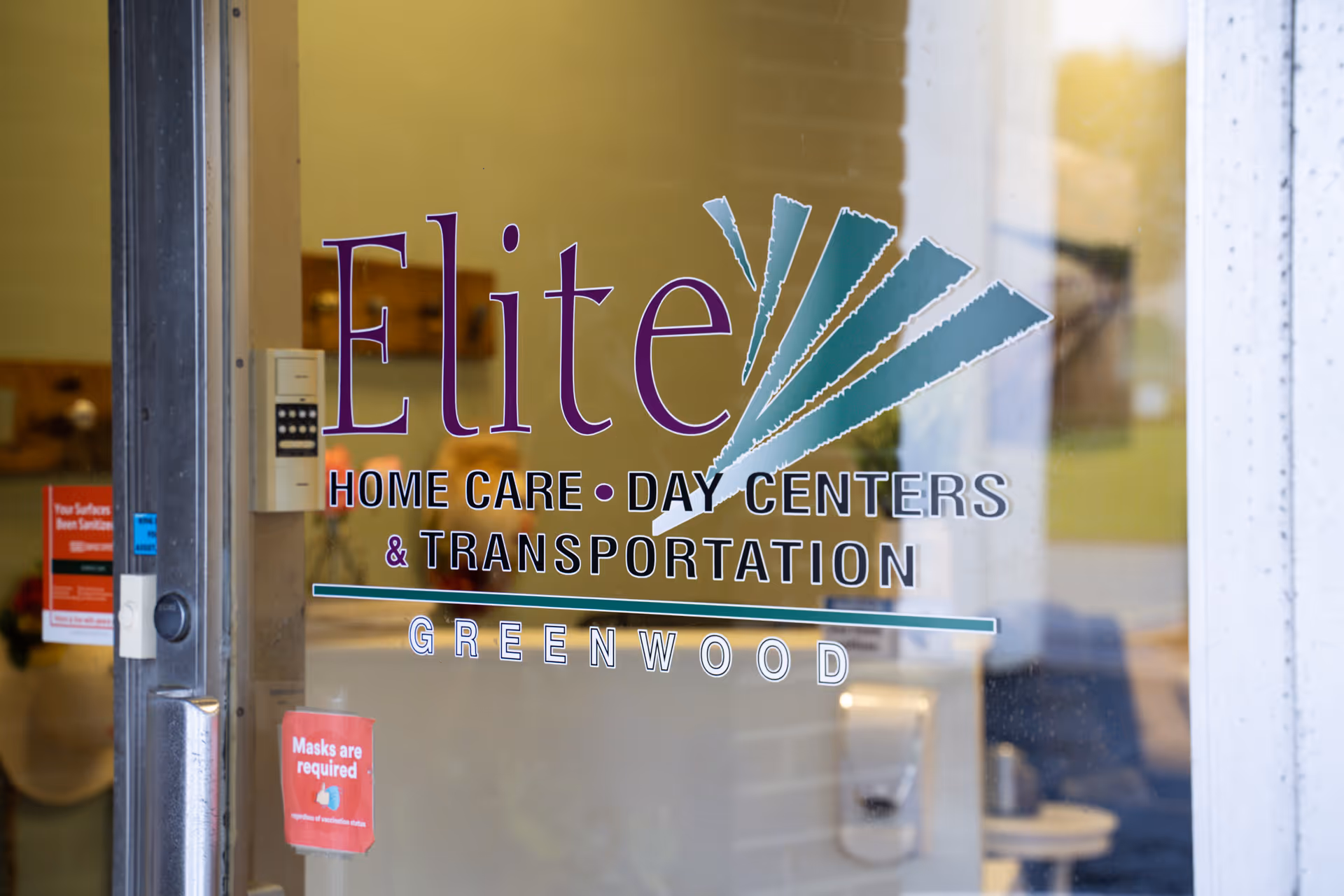 Glass entrance door with Elite Home Care Day Centers branding and Greenwood location on glass.