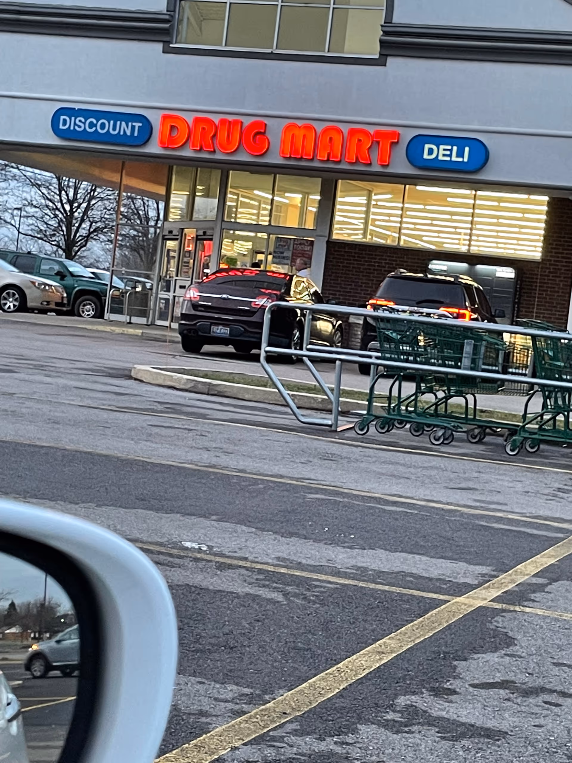 Front of Discount Drug Mart store with red neon sign and shopping carts in parking lot.