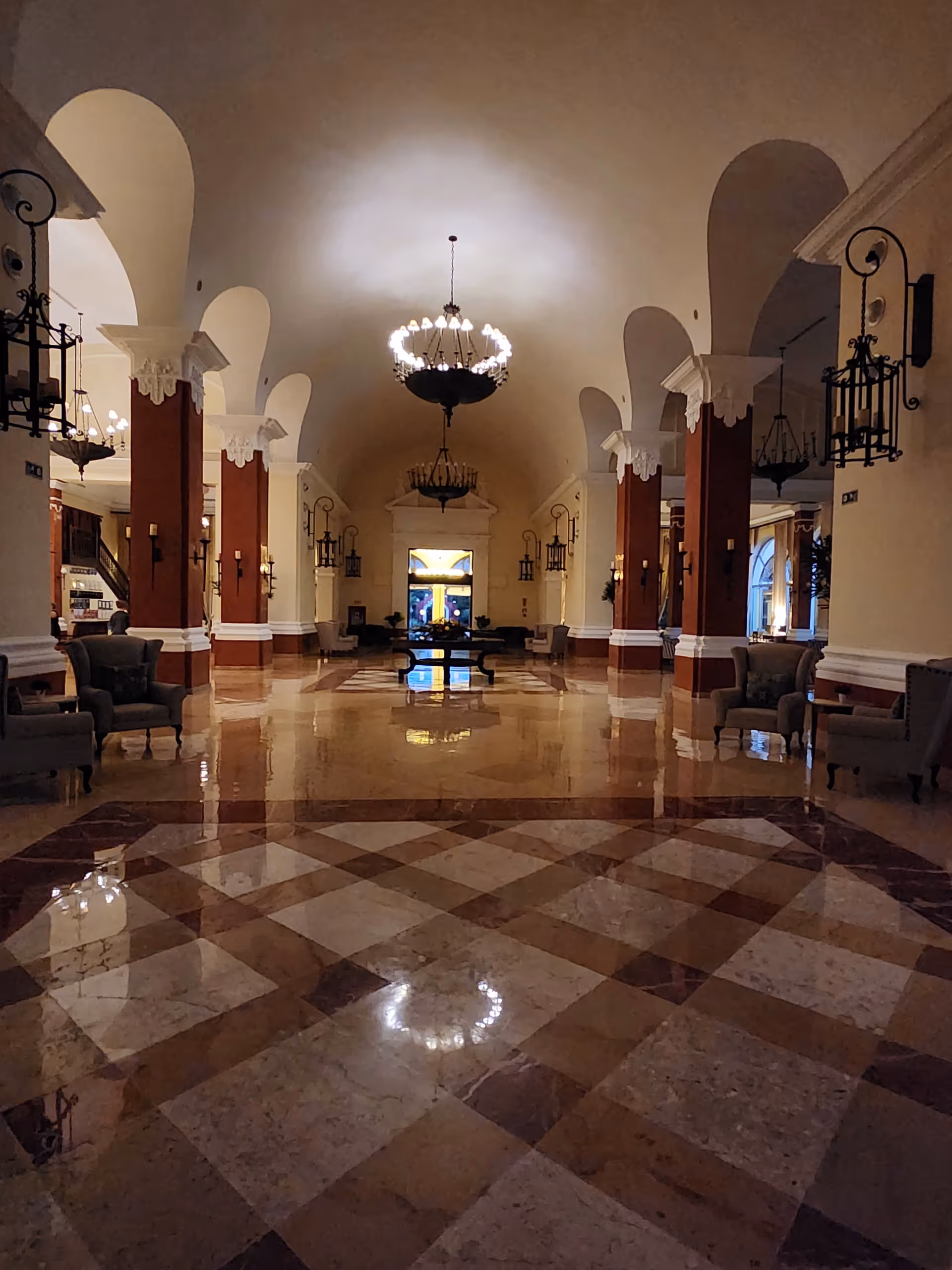 Grand hotel-style lobby with arches, chandeliers, and marble tiled floor.