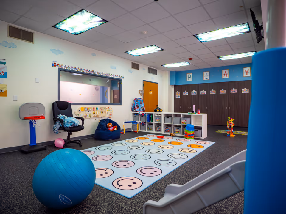Bright children's playroom with toys, storage cubbies, a slide, and a smiley-face rug.