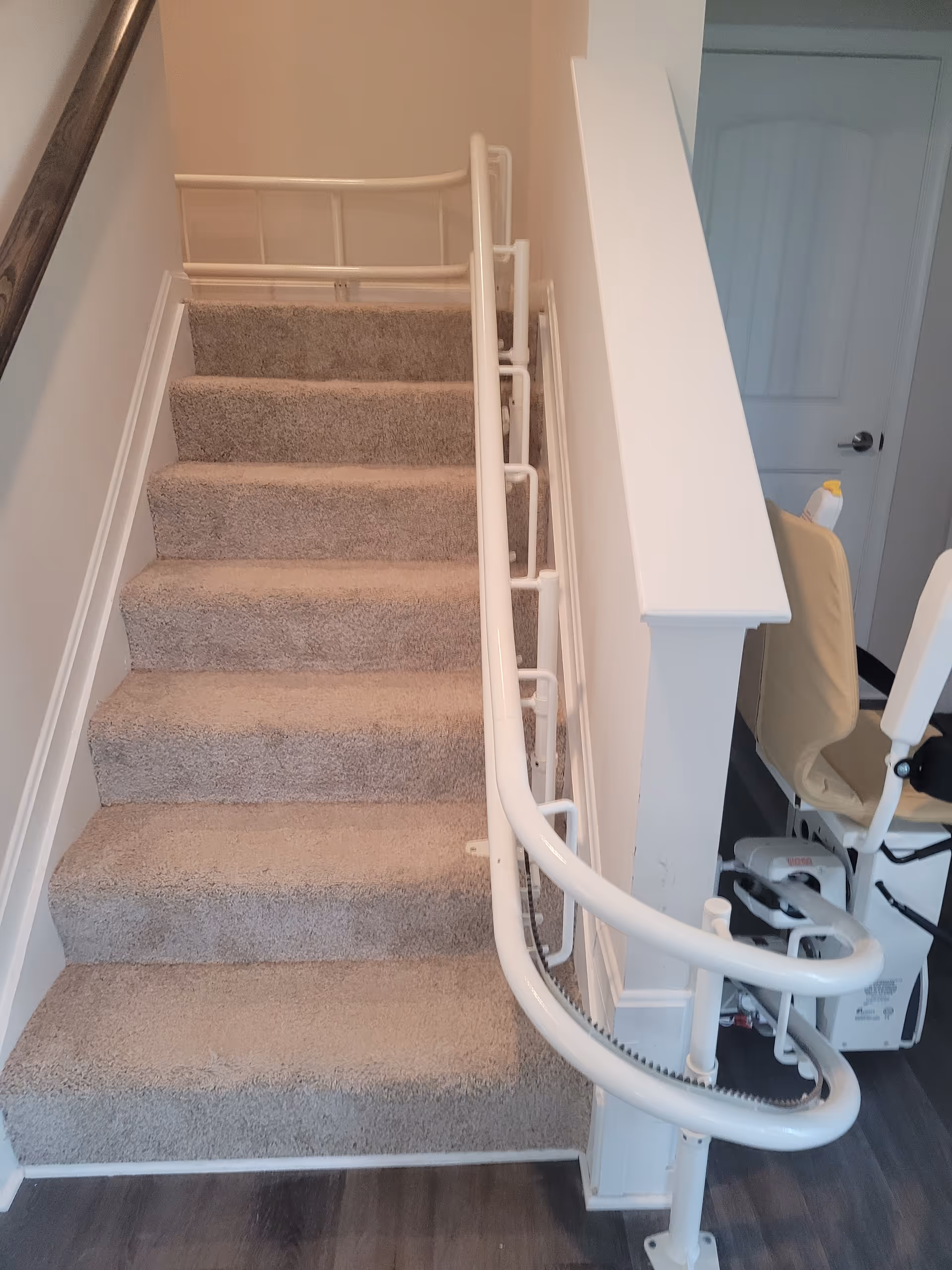 Interior staircase with carpeted steps and a white curved stairlift rail along the banister.