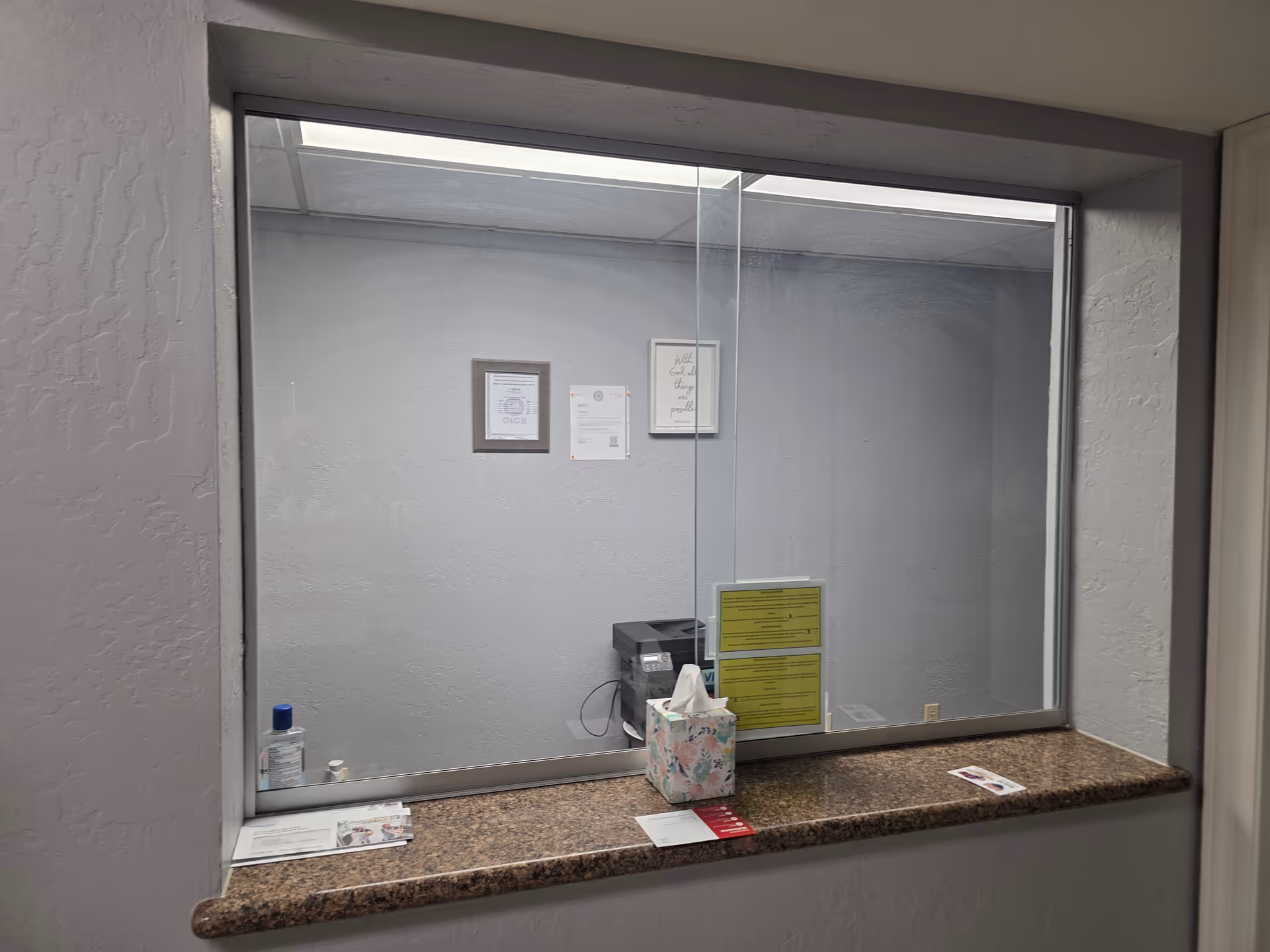 A reception window with a granite counter and supplies inside a gray-walled room.