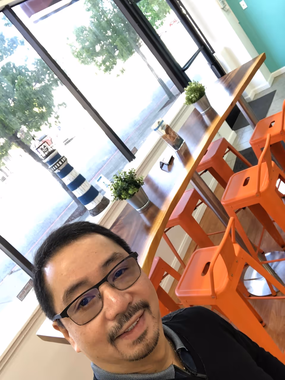 Self-portrait of a man in Beacon Home Care dining area with orange stools and plants.