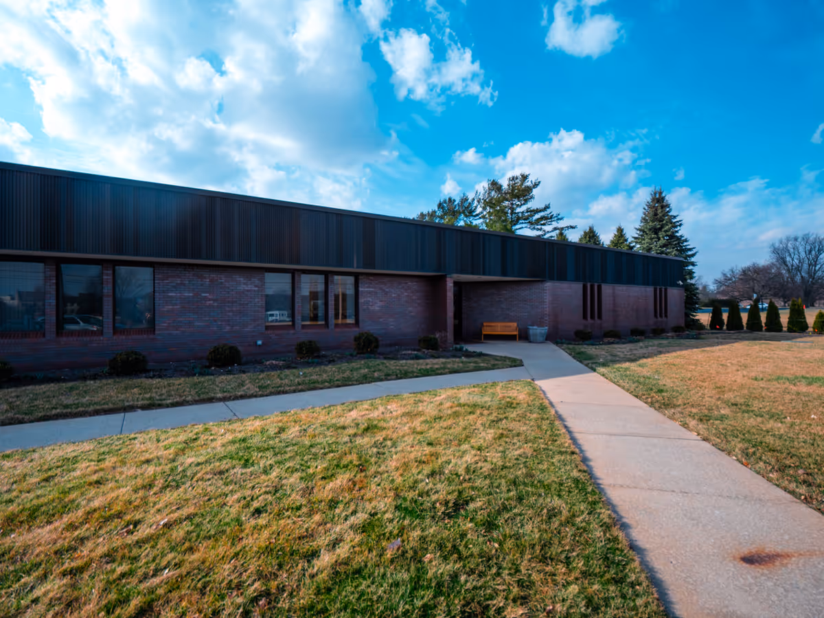 Exterior view of a brick senior living facility with a walkway and bench.