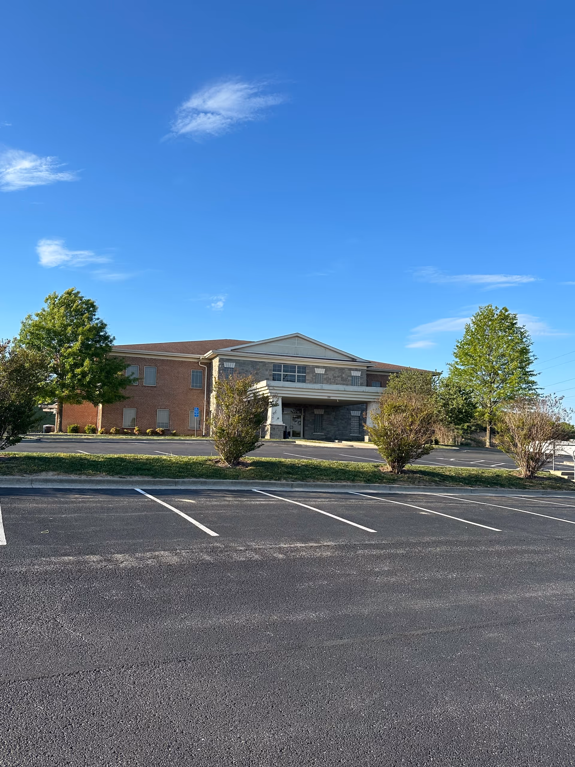 A brick senior living facility front with parking lot and blue sky.
