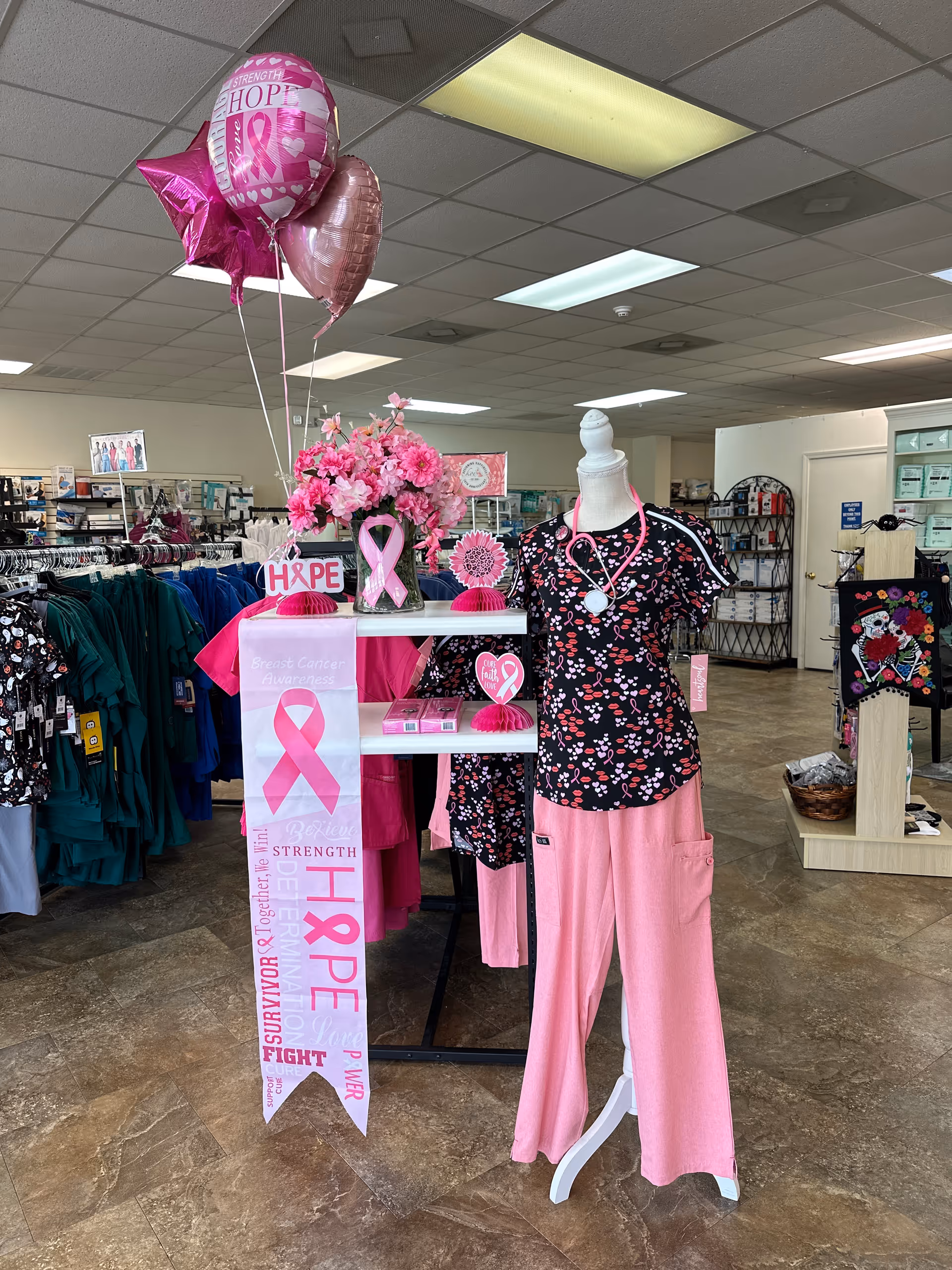 Indoor store-style space with pink breast cancer awareness decor, balloons, and clothing on mannequins.
