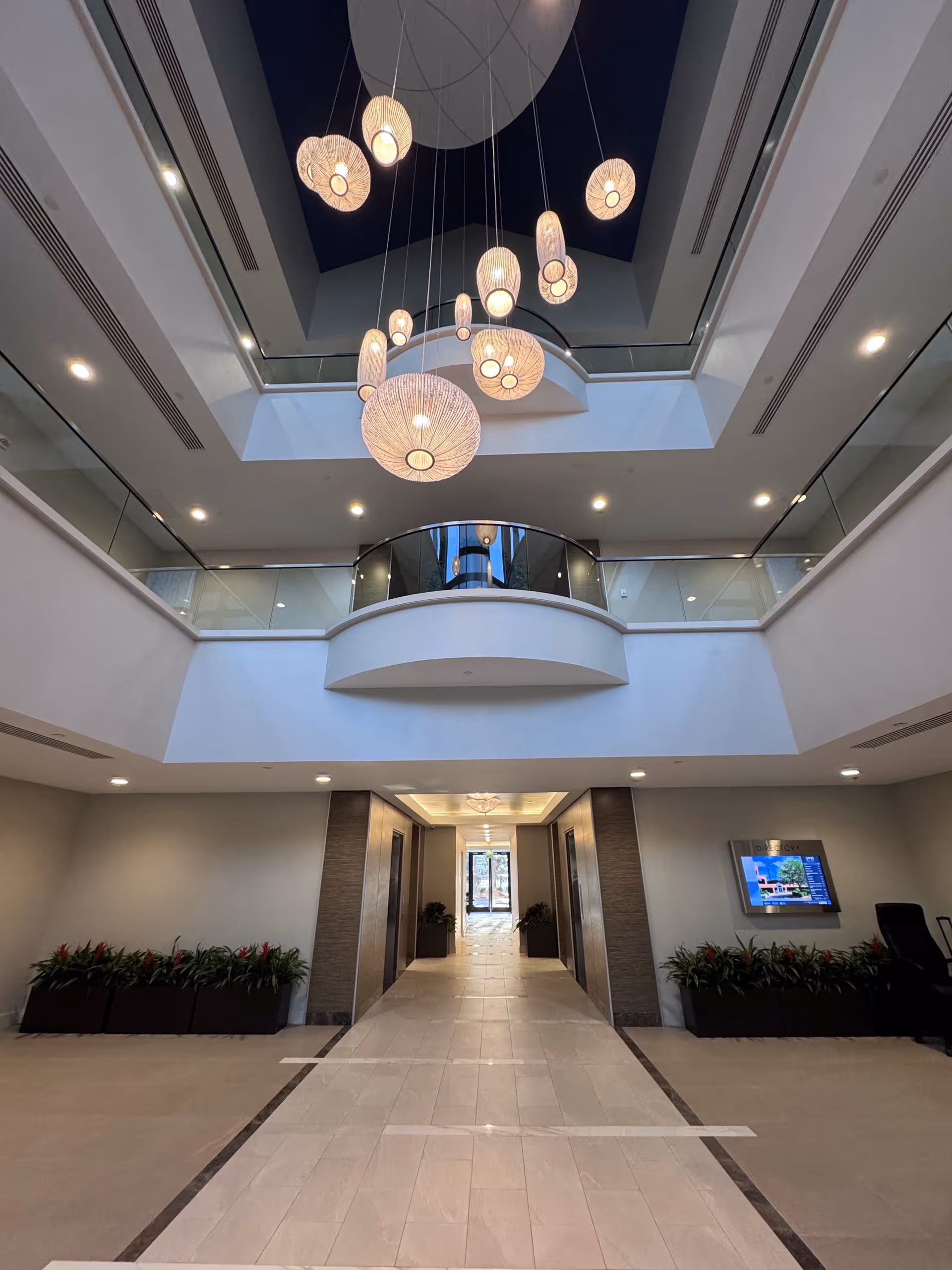 Interior atrium lobby with pendant lights, corridor, and planters.