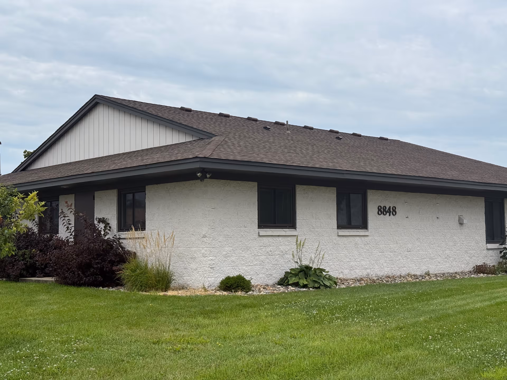 Single-story building exterior with light walls, dark trim, and a manicured lawn.