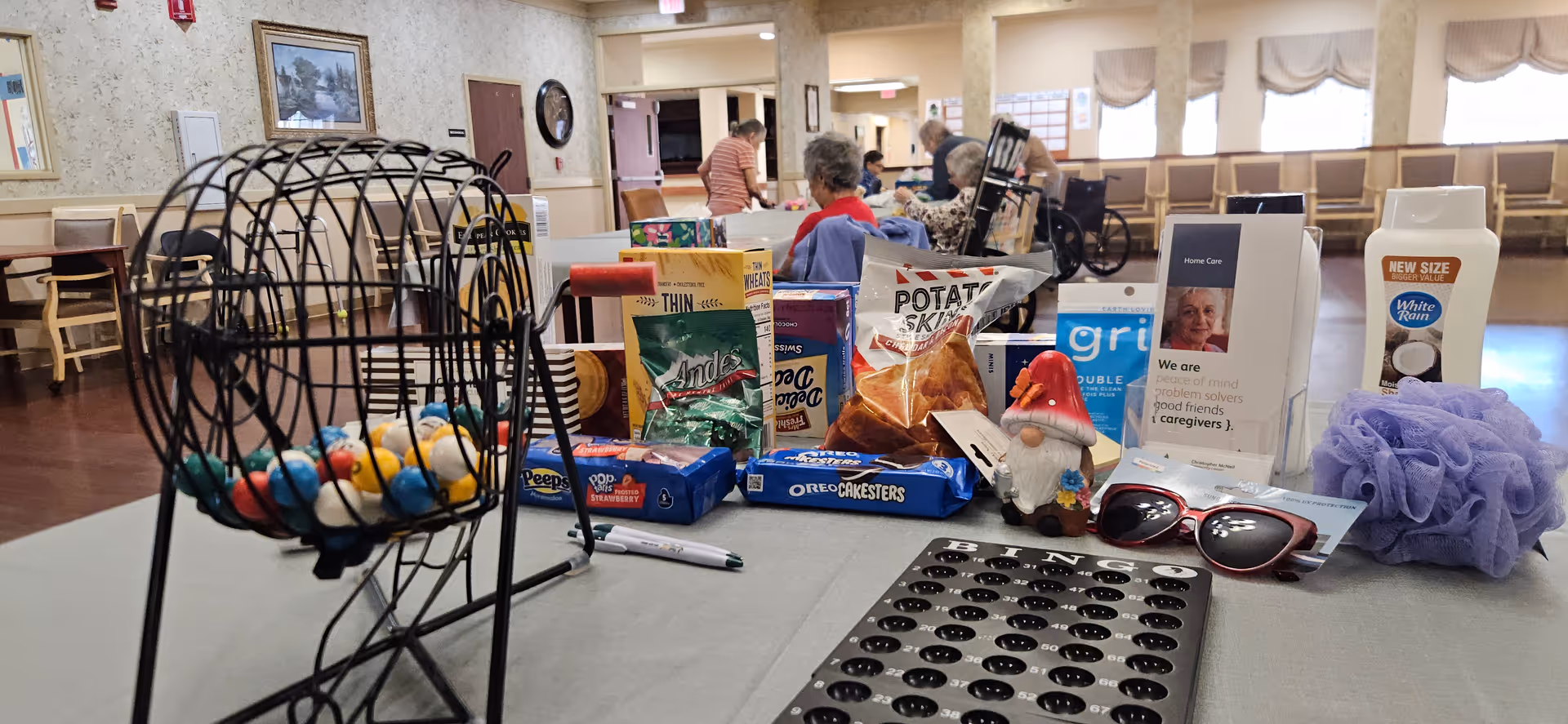 Indoor senior living common area with a table of snacks, game items, and residents.