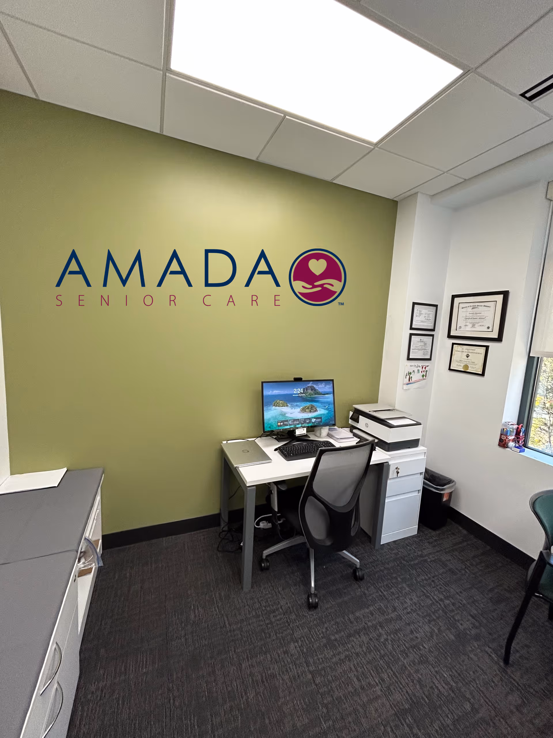 Amada Senior Care office with desk, computer, printer, and framed certificates.