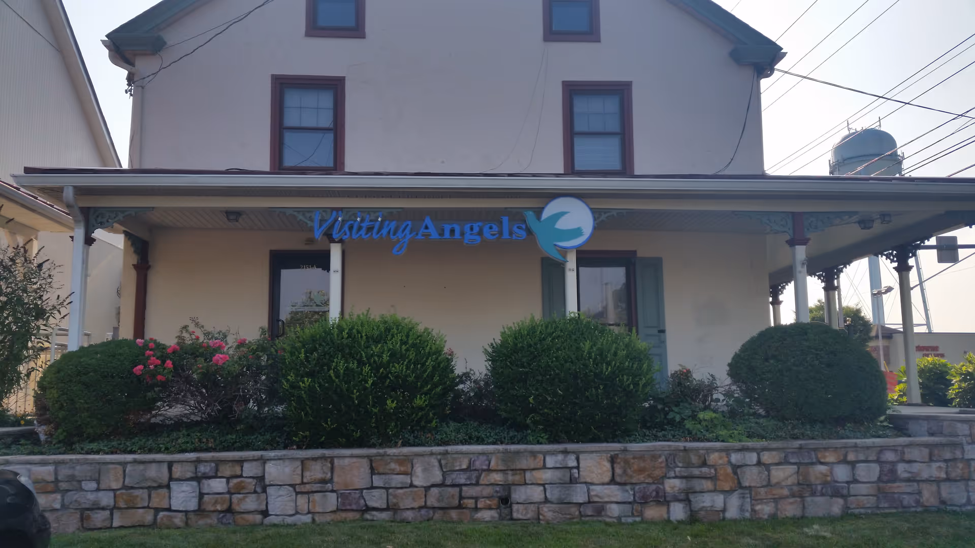 Exterior view of Visiting Angels senior home care building with bushes and a stone wall.