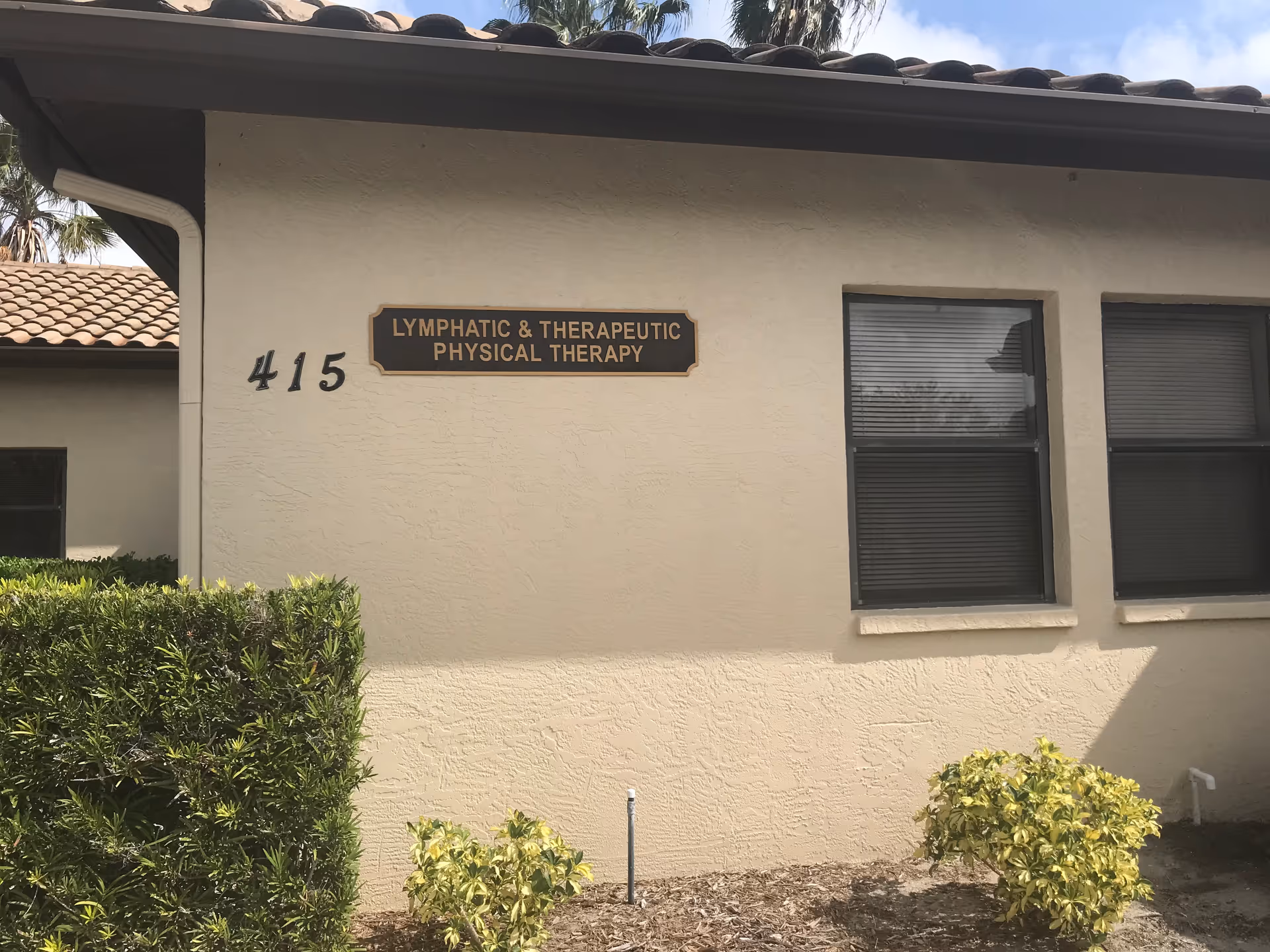 Exterior view of a beige facility with a sign for Lymphatic & Therapeutic Physical Therapy.