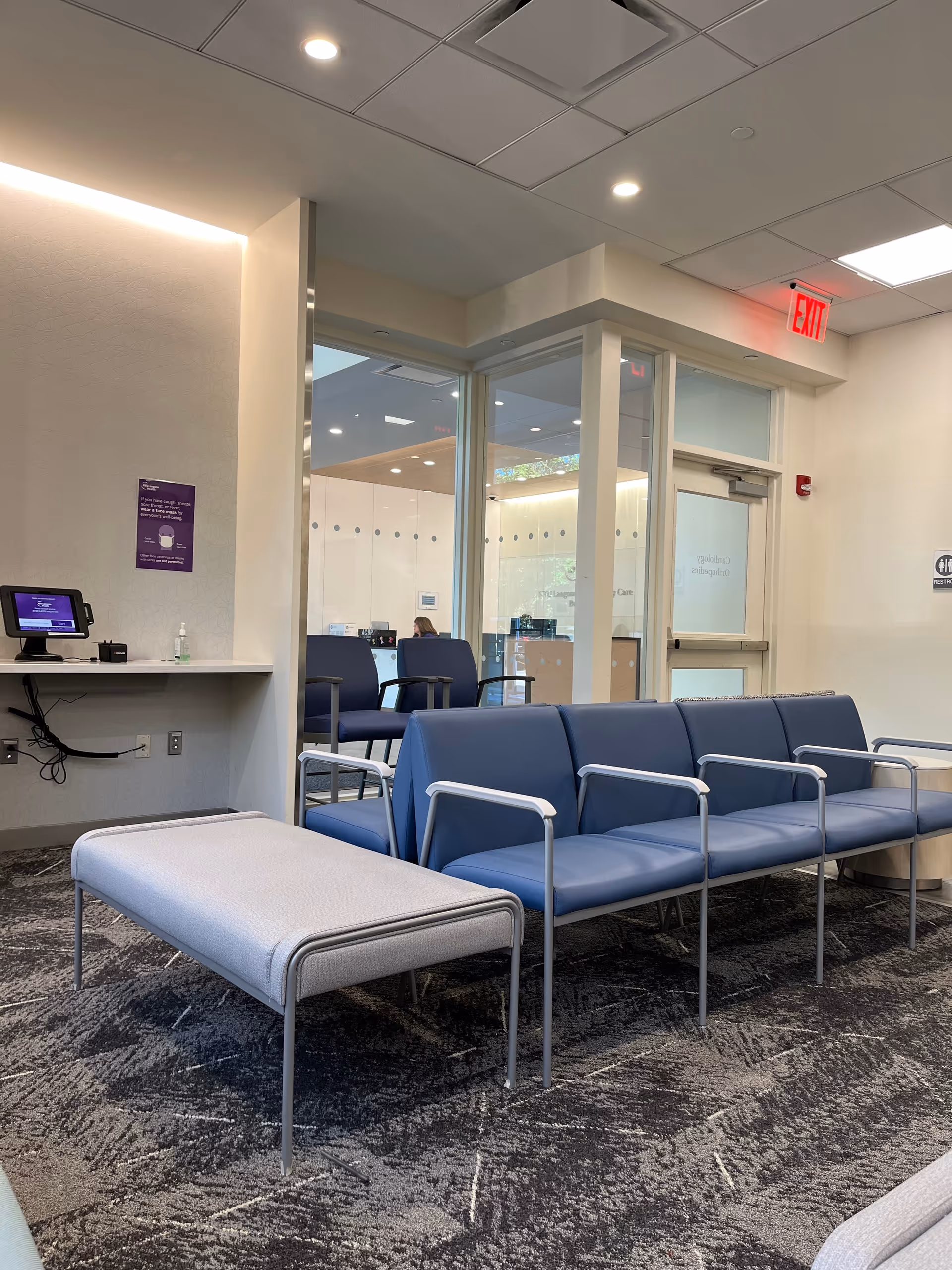Ambulatory care waiting area with blue seating and glass doors.