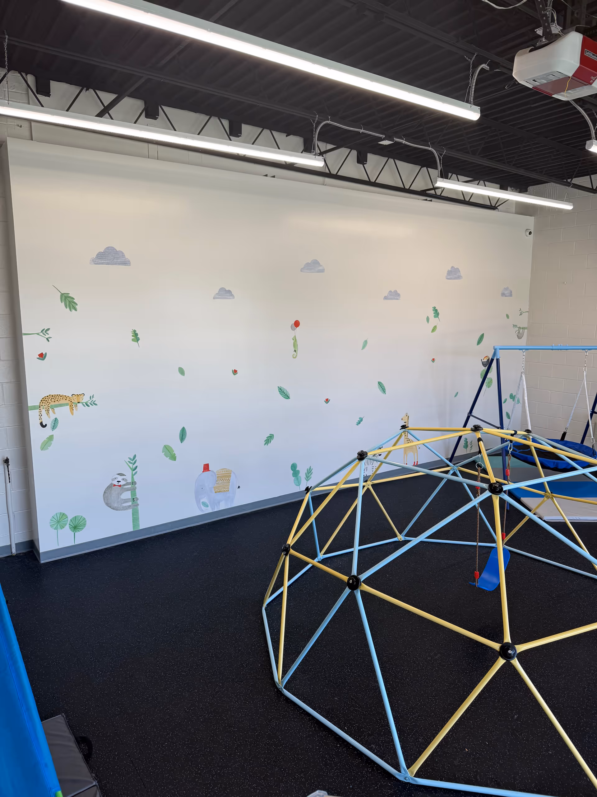 Indoor playroom features a geodesic climbing dome and mural-covered wall.