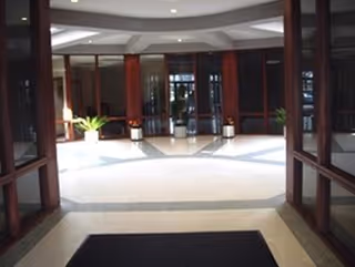 Bright interior lobby with glass doors, red columns, and potted plants.