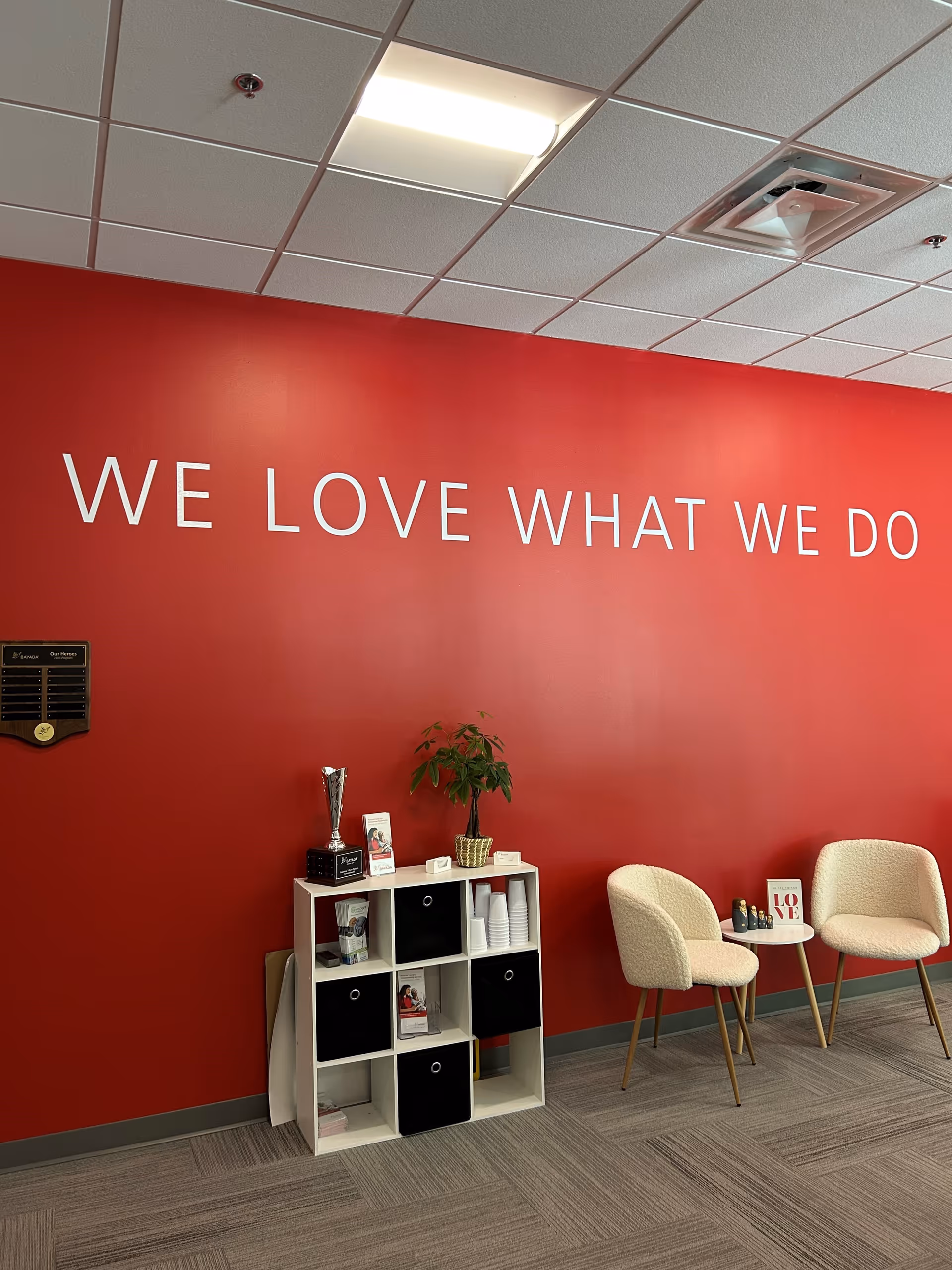Red lobby wall with white shelving, plant, and two beige chairs in a waiting area.