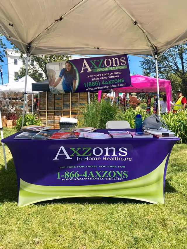 Outdoor promotional booth for Axzons Home Care with banners, pamphlets, and a purple tablecloth.