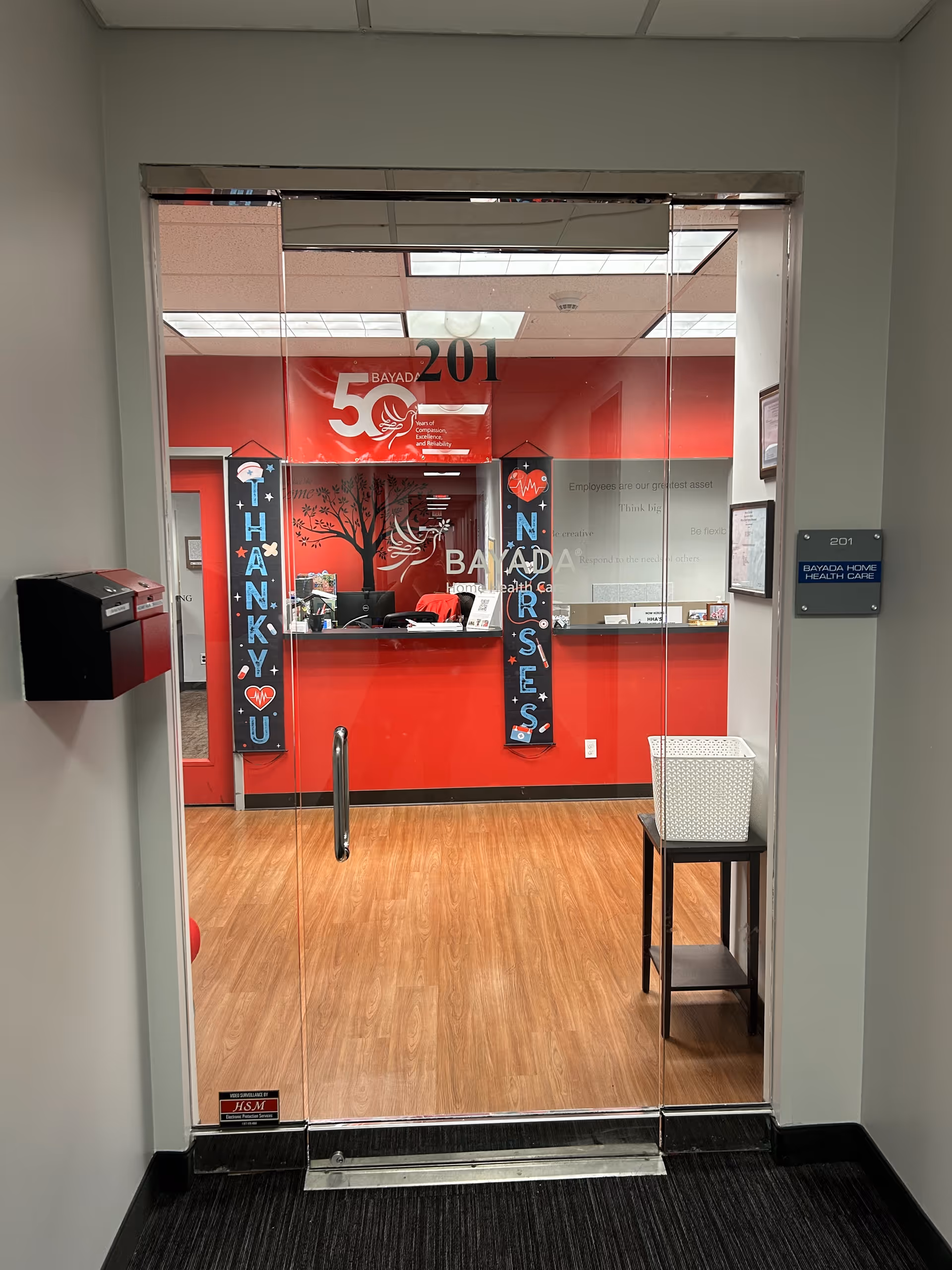 Glass entrance doors open to a red BAYADA reception area with a desk and banners.
