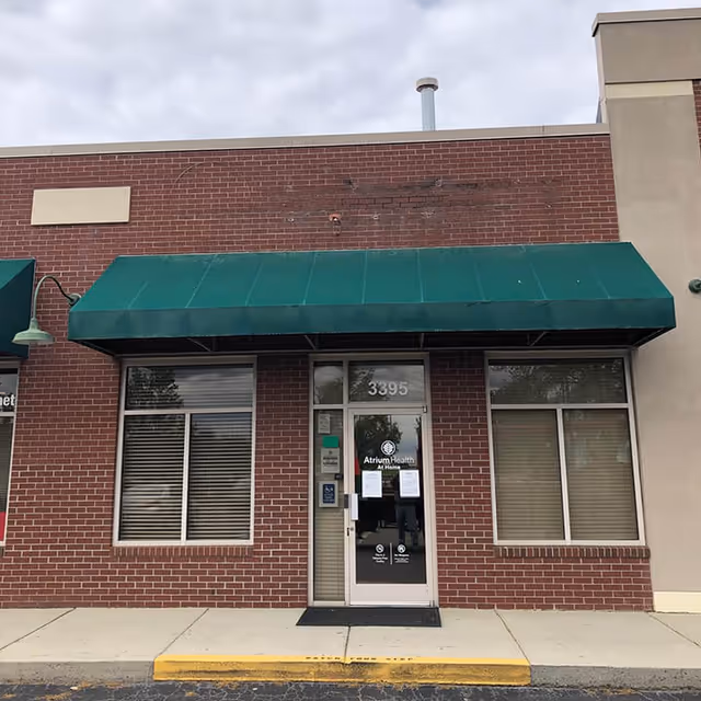 Brick storefront with a green awning and glass door labeled Atrium Health At Home.