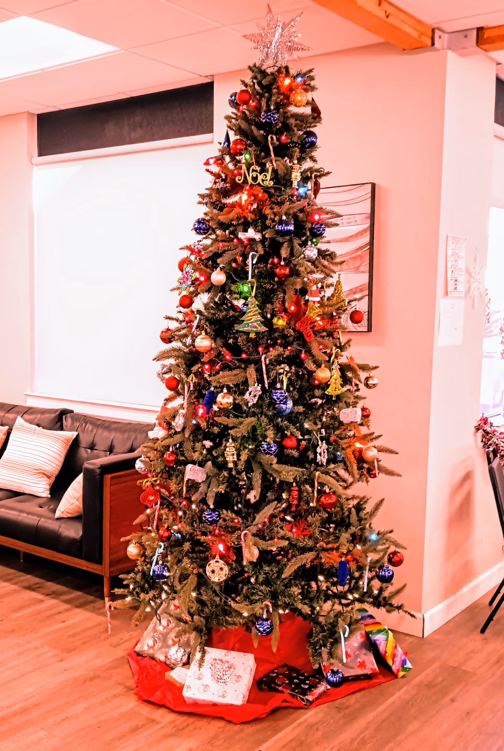 A decorated Christmas tree with presents sits in a cozy indoor facility lounge.