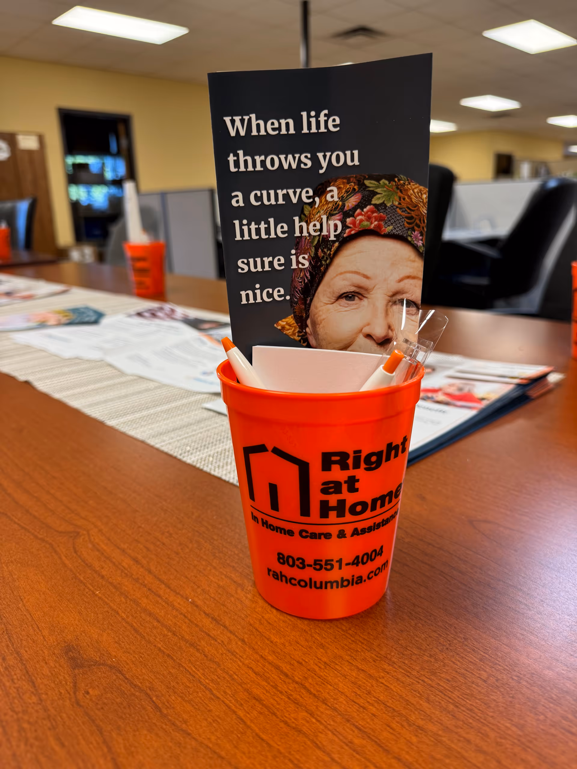 Orange Right at Home promotional cup beside a brochure featuring an elderly woman.